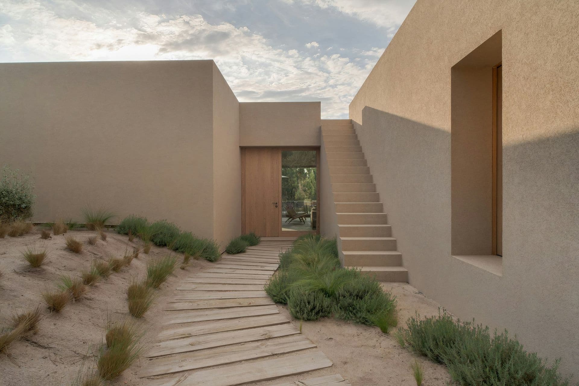 Sand-rendered facade with an external stair and boardwalk path at Mighty Pine