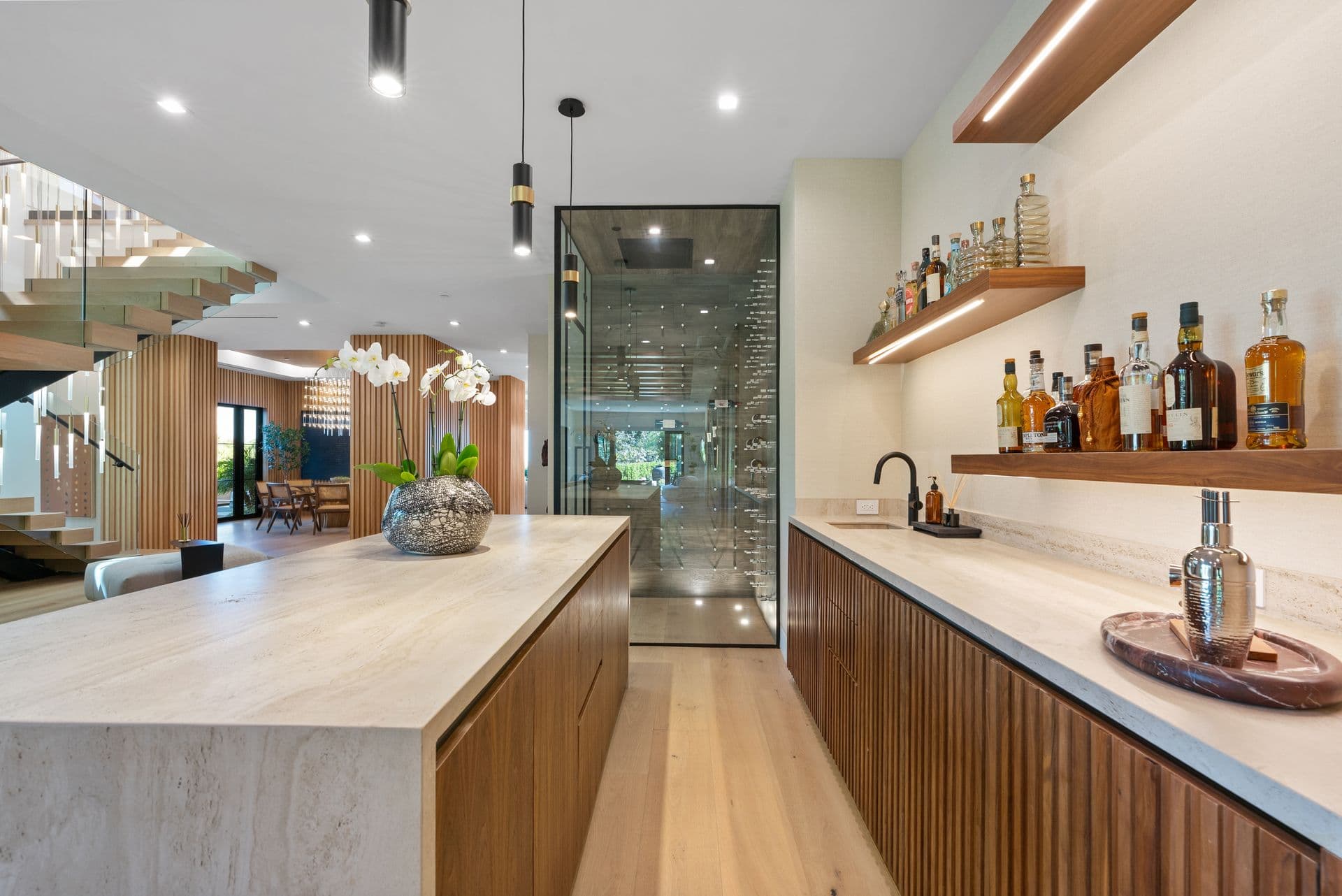 Home bar with backlit spirit shelves beside the floating staircase at Bel-Air Oasis, Los Angeles