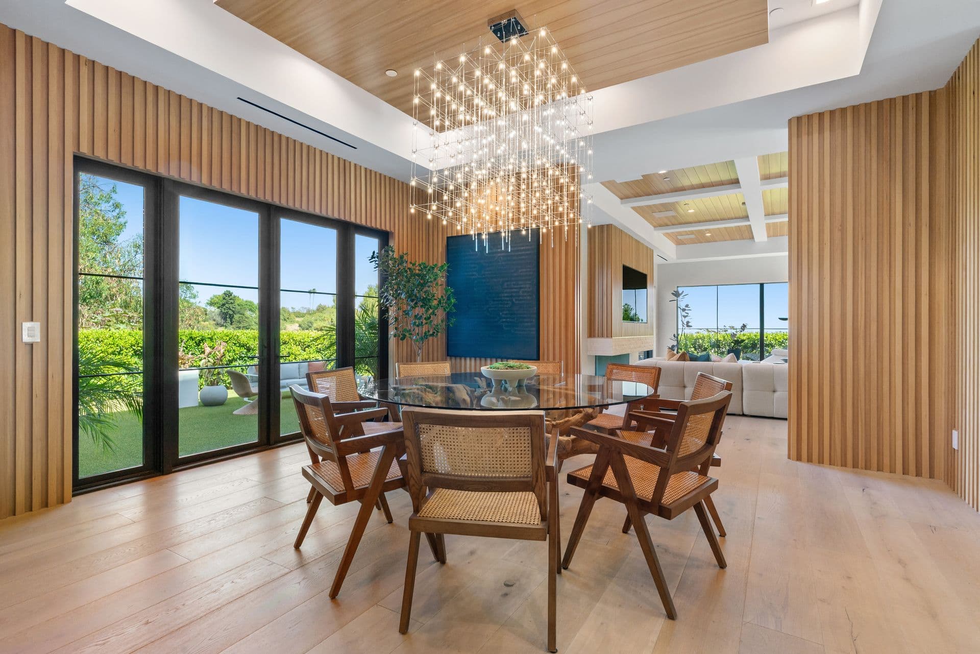 Dining room with a glass table and cascading chandelier under a timber ceiling at Bel-Air Oasis, Los Angeles