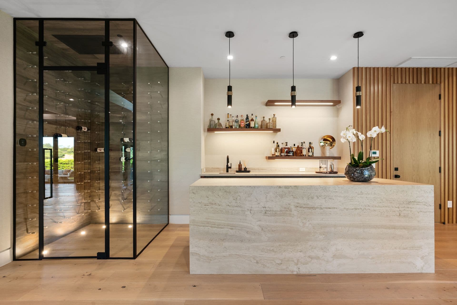 Glass-walled wine room beside a travertine bar at Bel-Air Oasis, Los Angeles