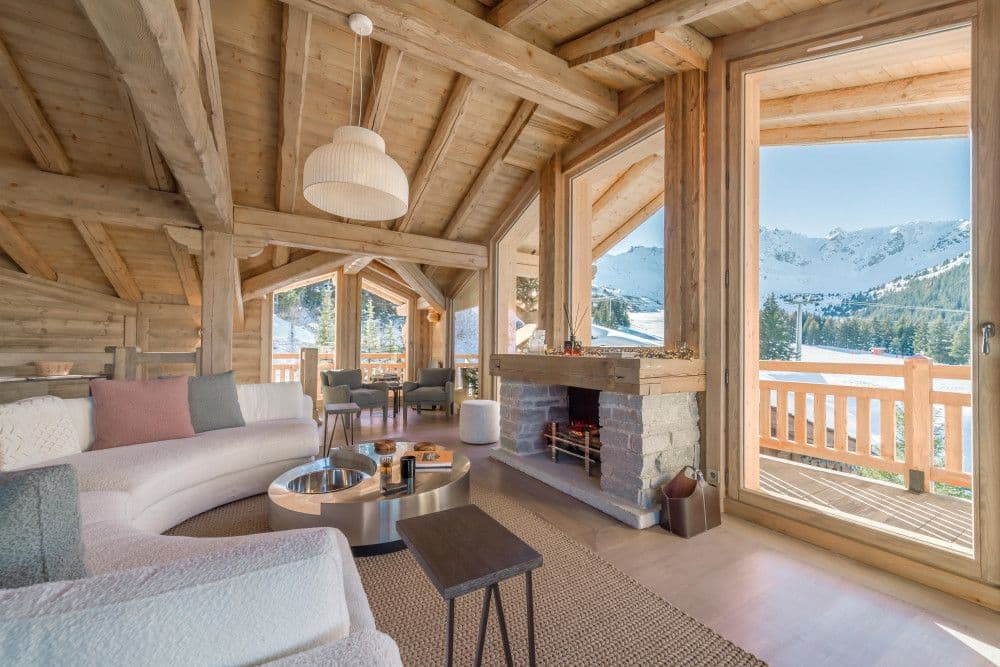 Living room with a fireplace and curved sofa opening to a mountain balcony at Courchevel 13