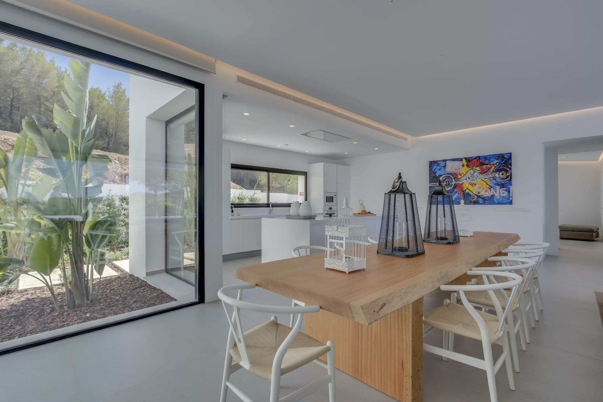 Dining table with wishbone chairs beside a glass corner and the kitchen at Dancing Shadows, Ibiza