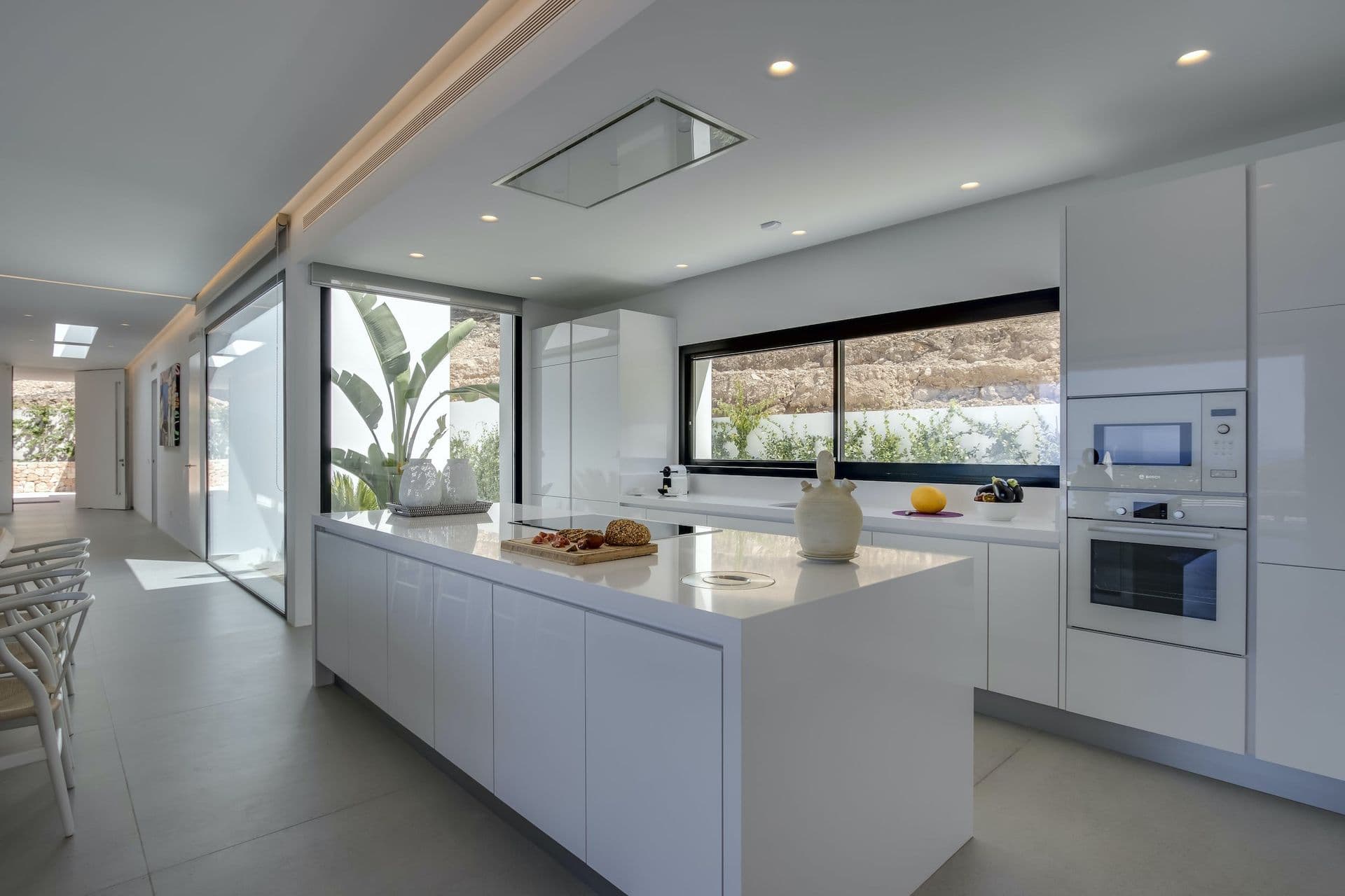 White kitchen with an island and a long window onto the hills at Dancing Shadows, Ibiza