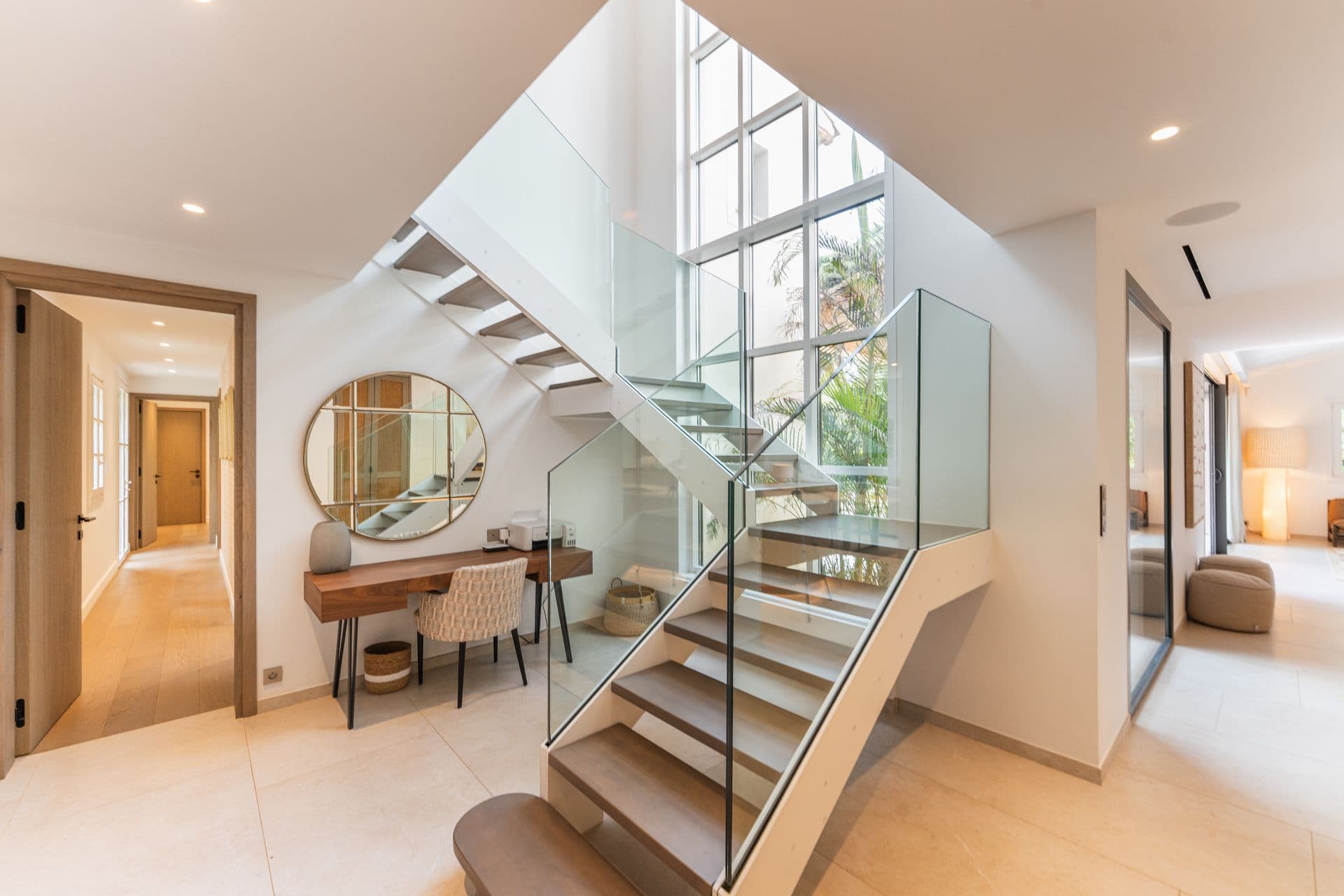 Entrance hallway with a floating staircase and a round mirror.