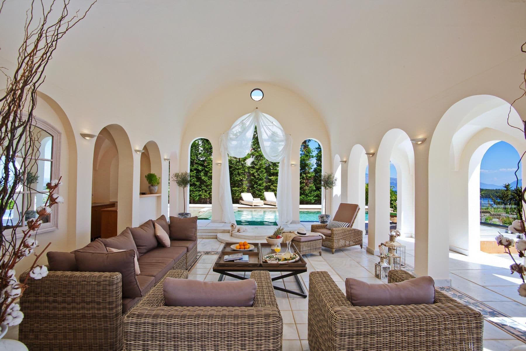 Arched stone loggia furnished with rattan sofas overlooking the pool