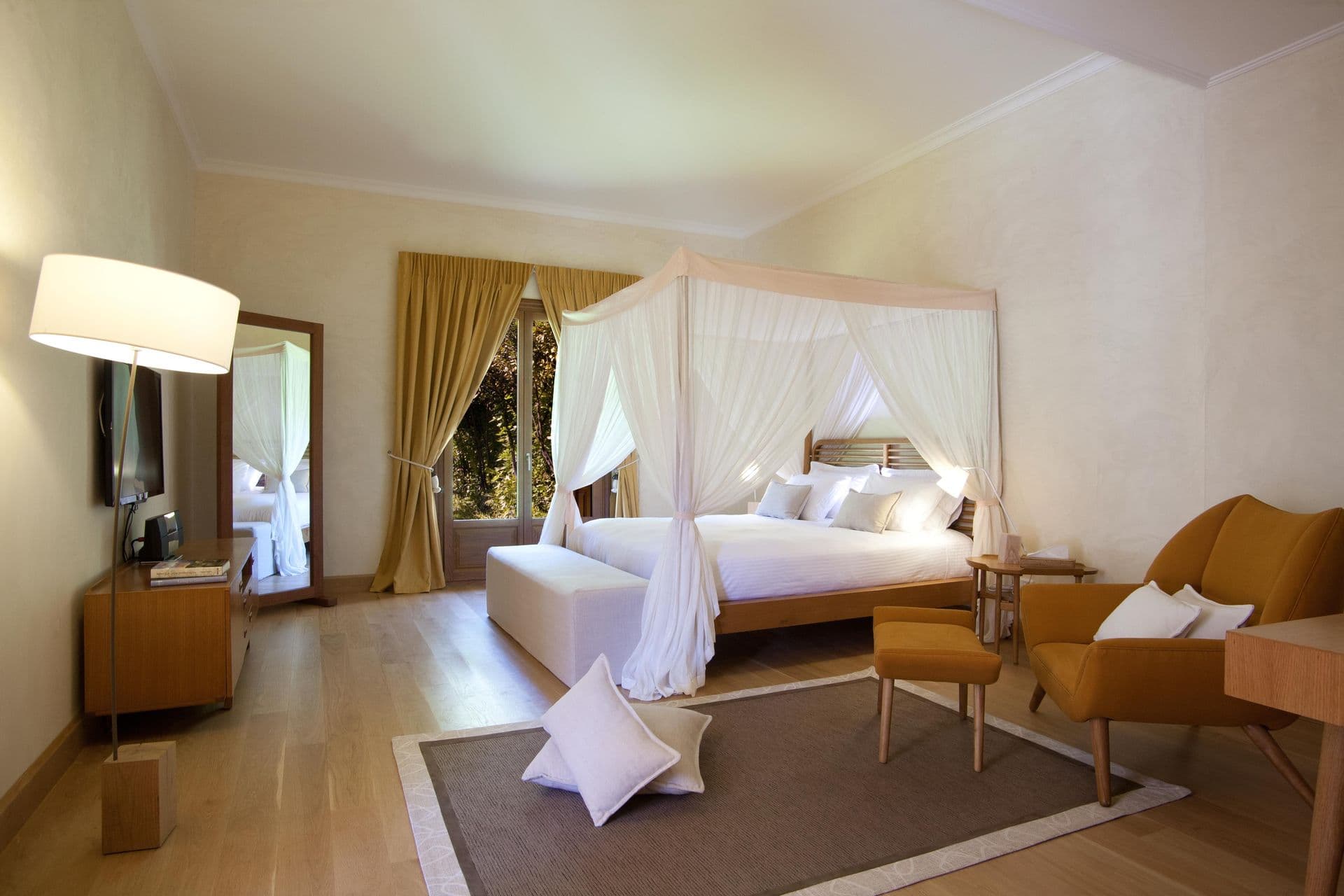 Bedroom with a white canopy bed, armchairs and warm lamplight
