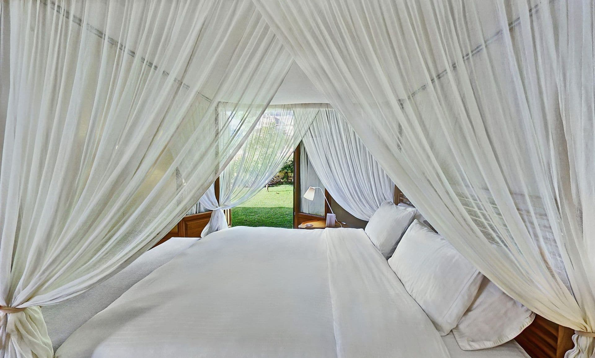 Bedroom with a sheer white canopy bed and garden-facing windows