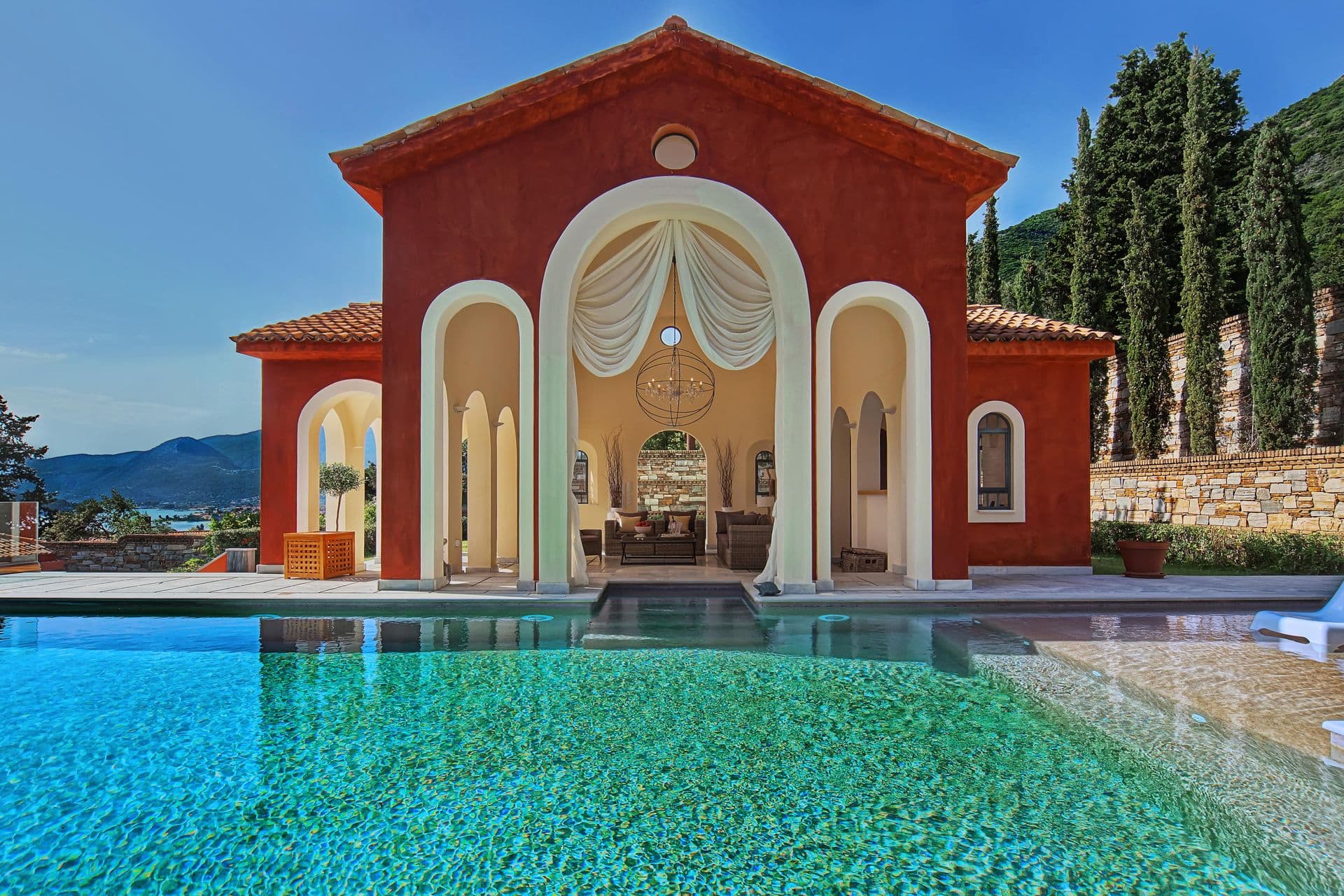 Ochre-red villa facade with arched windows and draped curtains beside the pool terrace