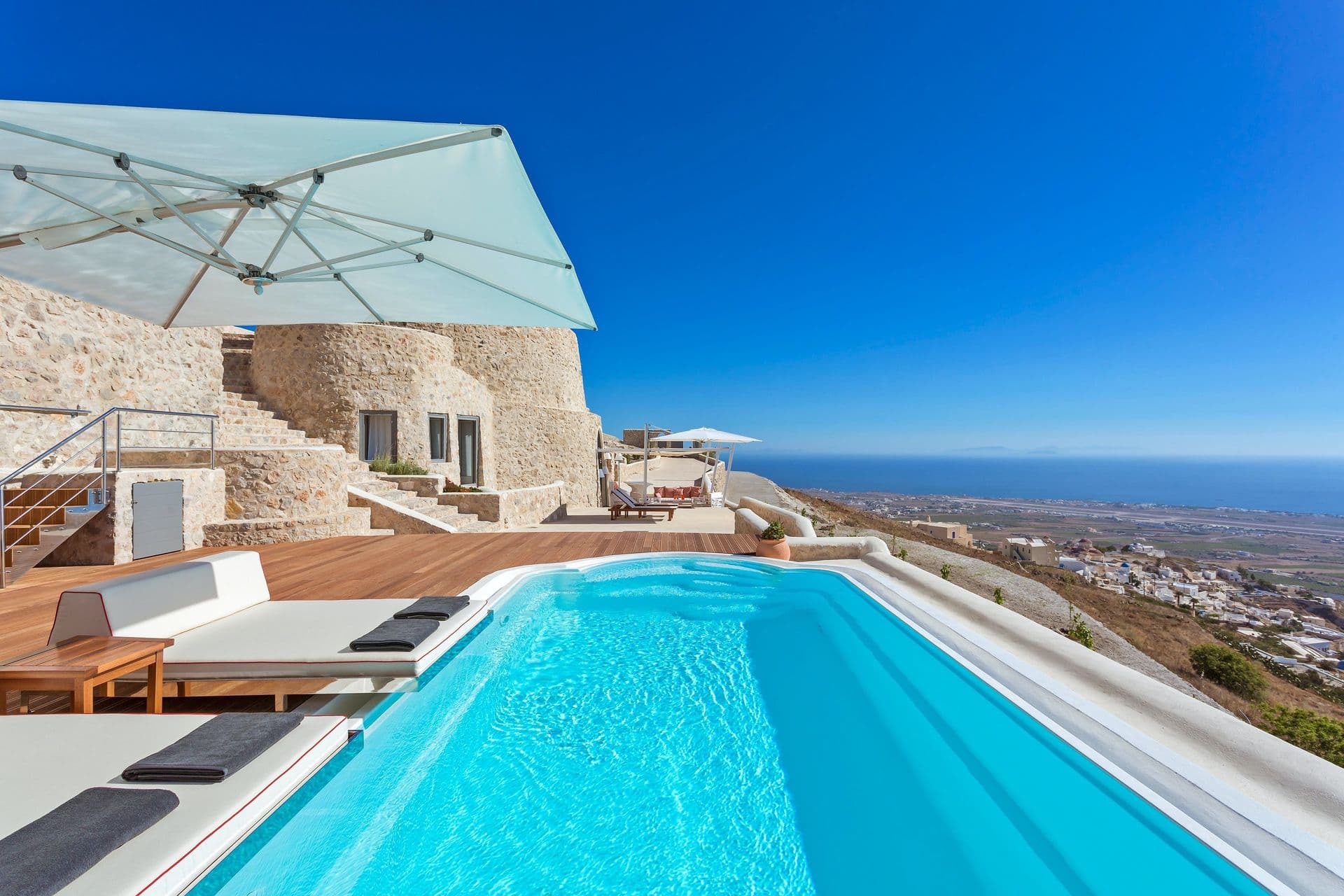 Infinity pool terrace with sun loungers overlooking the Santorini caldera.