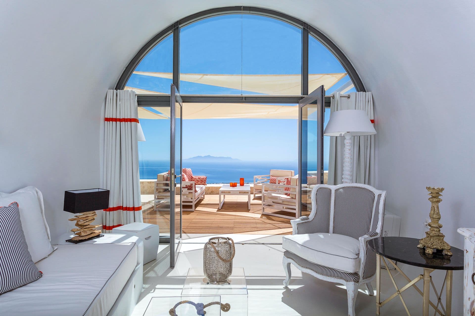 Living room with a curved arched window framing sea views, styled with red trimmed armchairs.