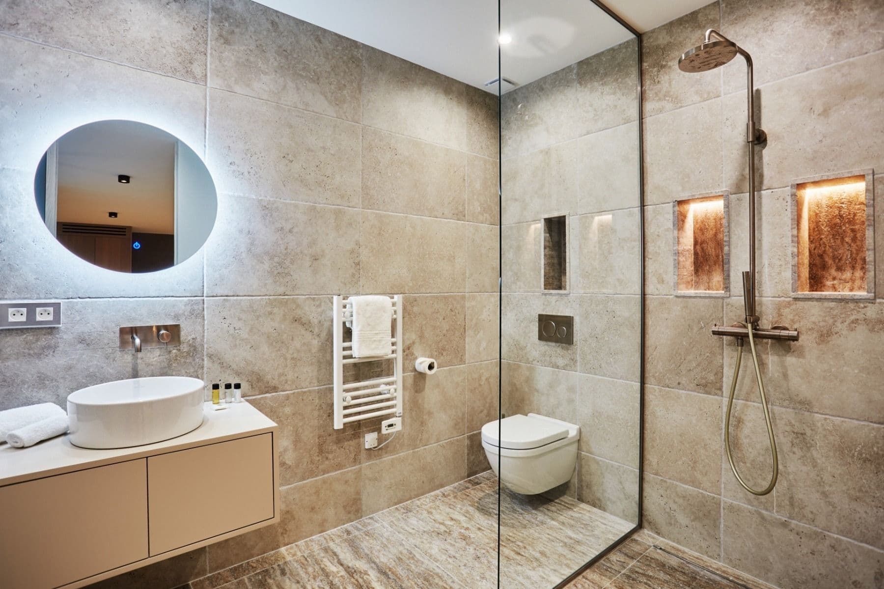 Bathroom with illuminated round mirror, floating vanity and rainfall shower
