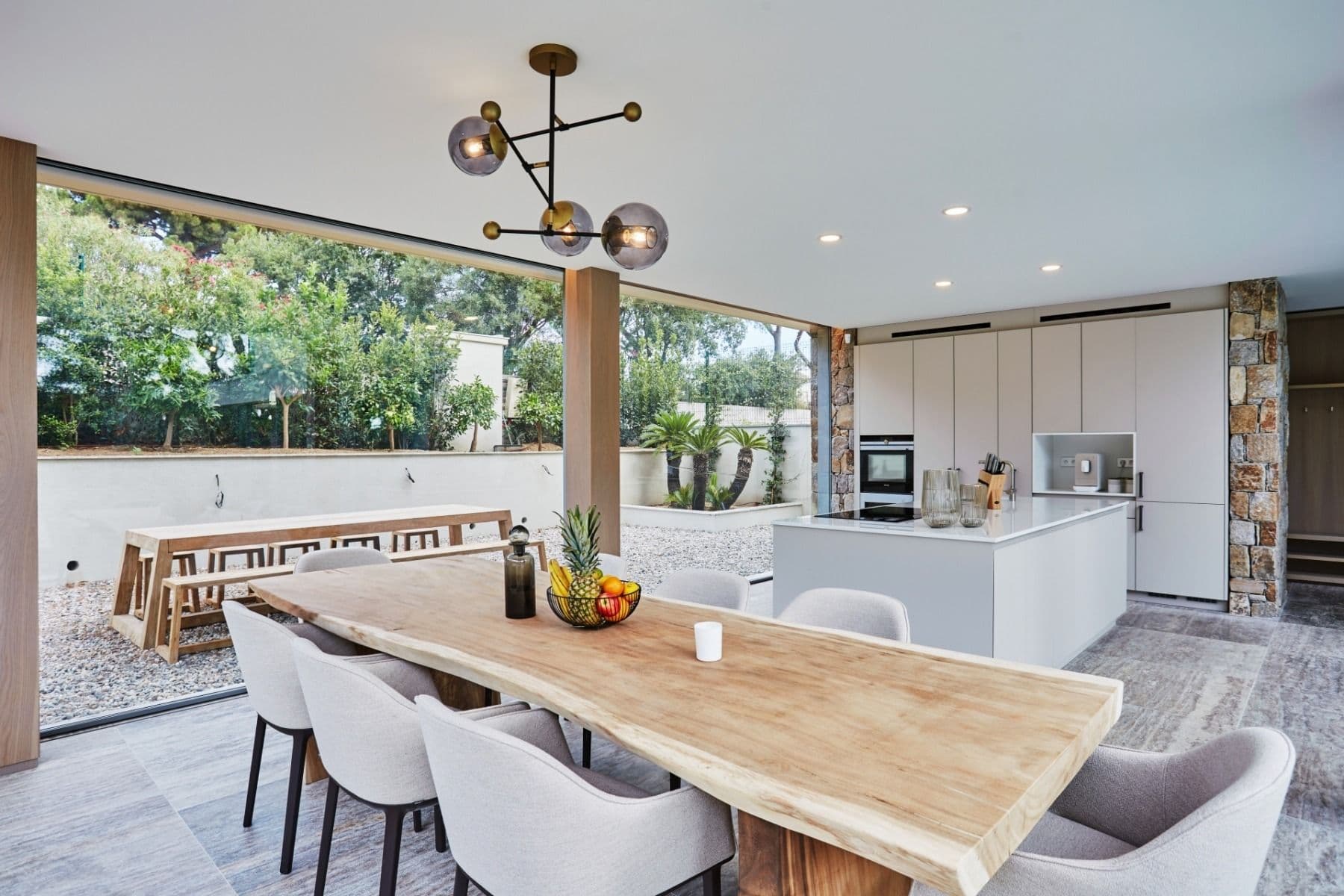 Covered outdoor dining area with wooden table opening onto the pool and lawn