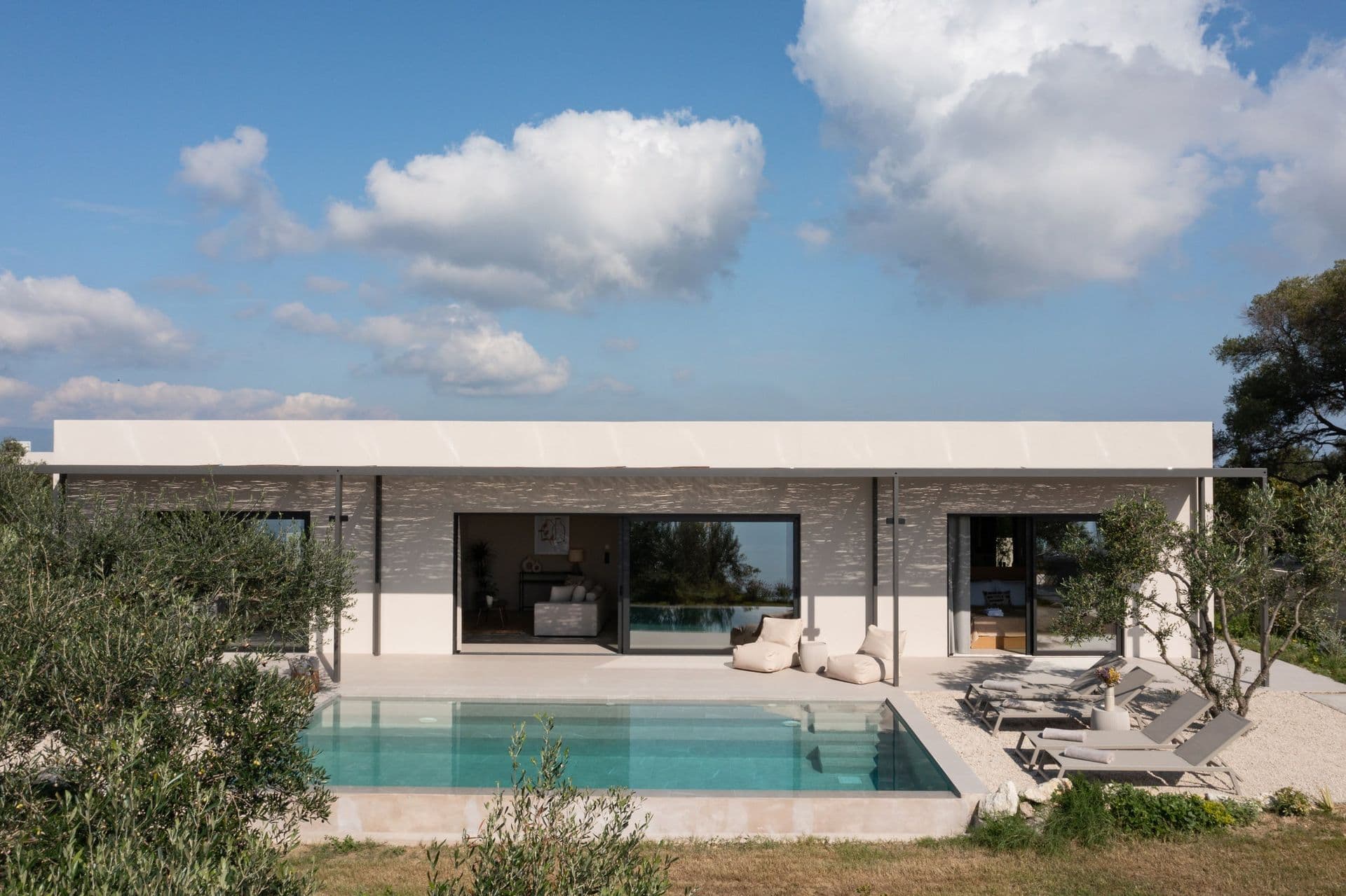 Stone-and-glass villa facade above the pool among olives at Corfu Dreams, Corfu