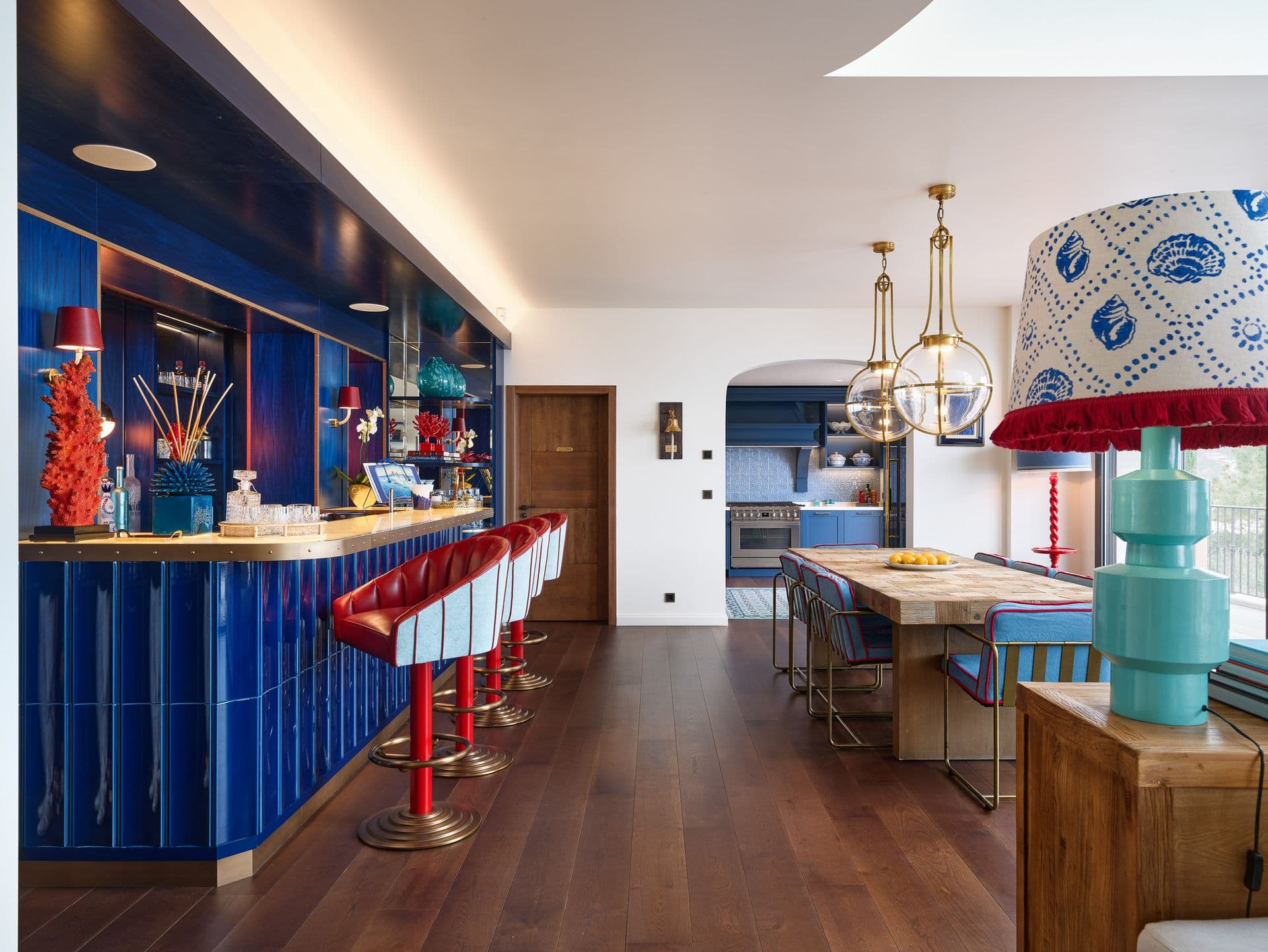 A cobalt blue home bar with red leather stools and glassware display