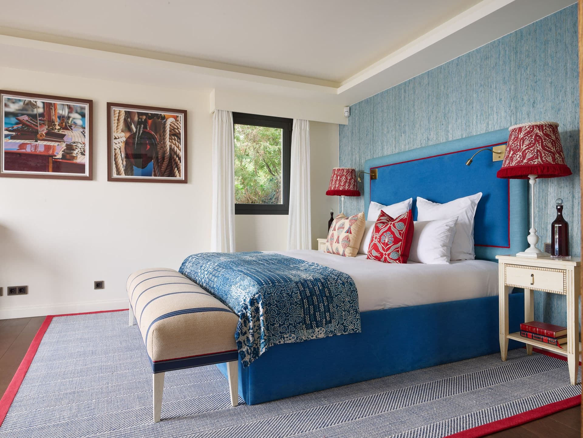 A bedroom with a navy upholstered headboard and red accent lamps