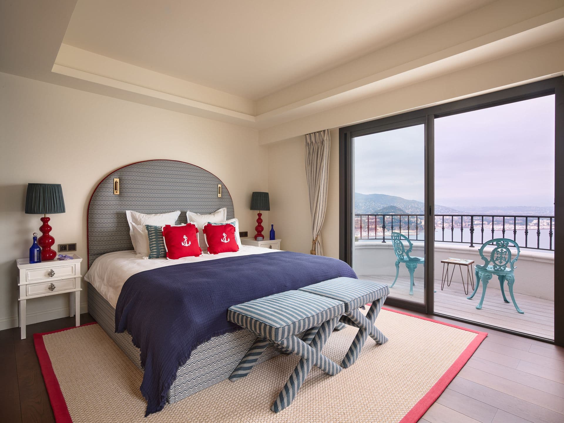 A bedroom with a teal throw and a picture window framing the sea view