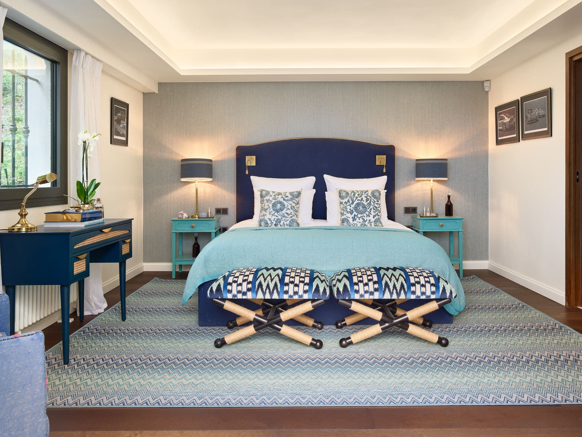 A teal and navy bedroom with a writing desk and matching bedside tables