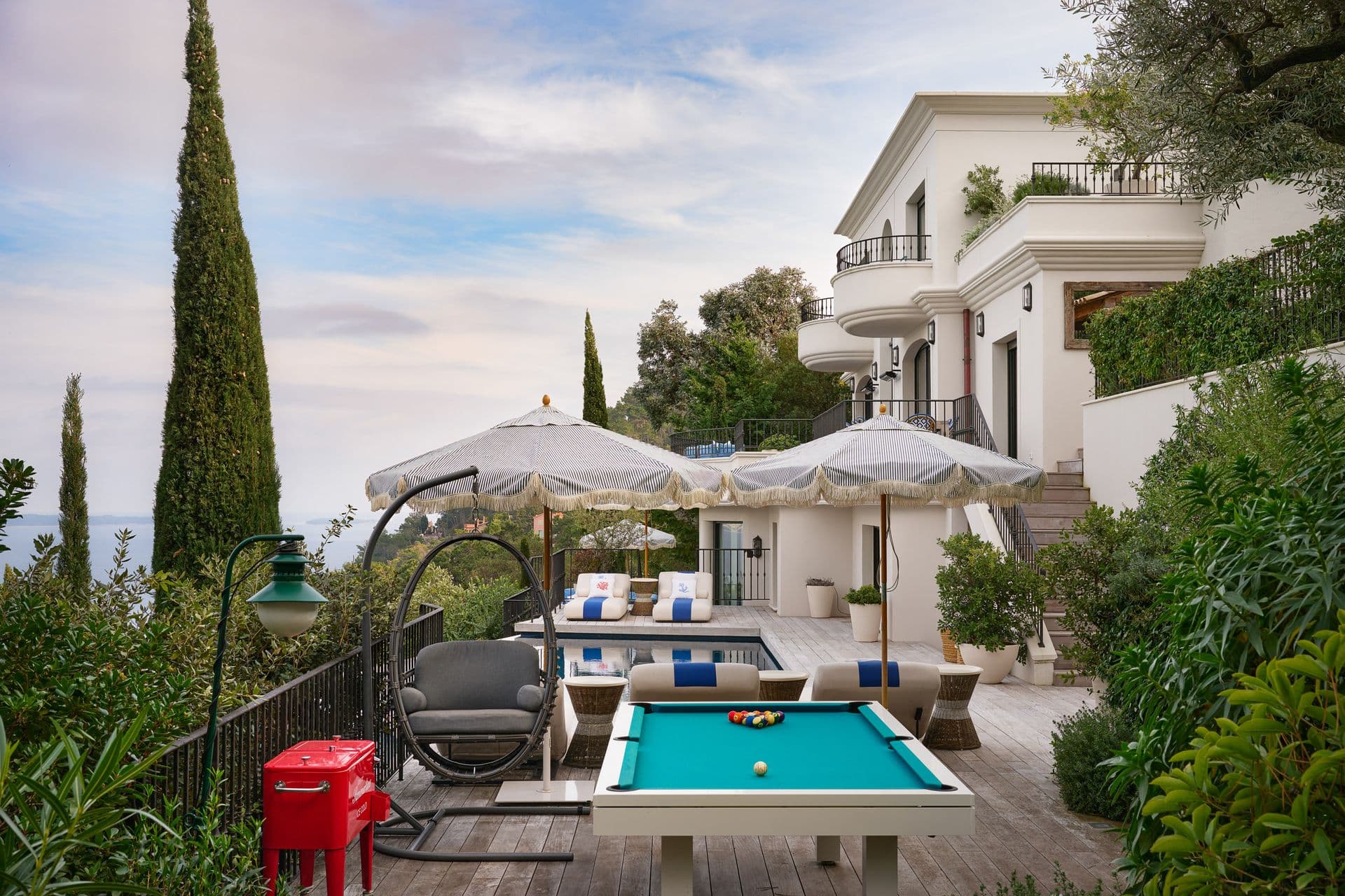 A landscaped terrace with a pool table and lounge seating among cypress trees