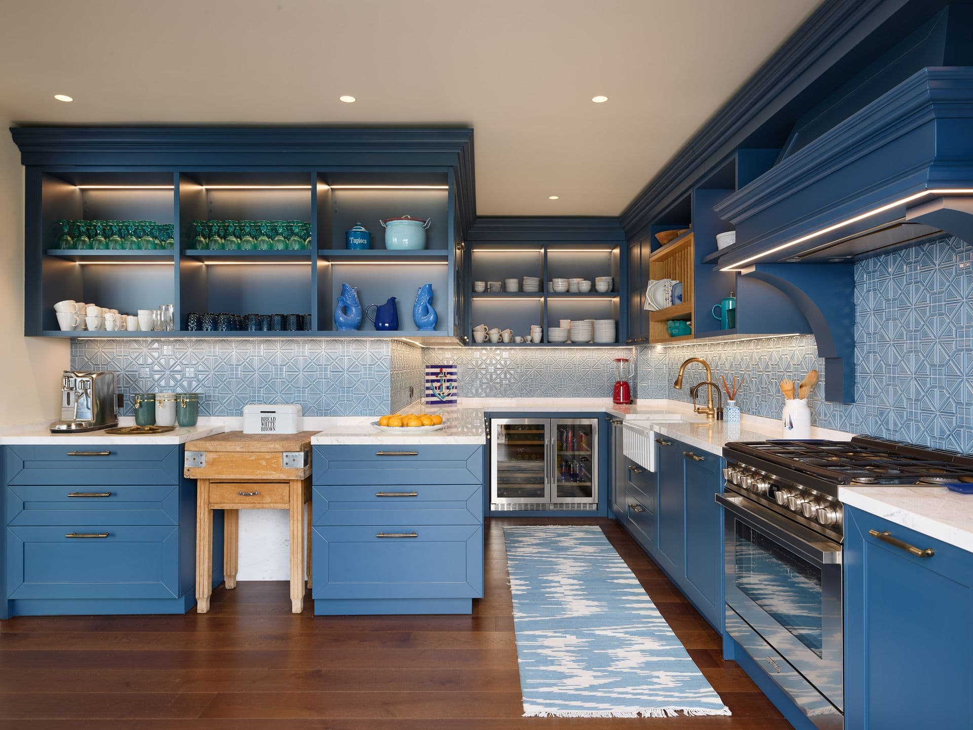 A navy blue kitchen with a large island and patterned runner rug