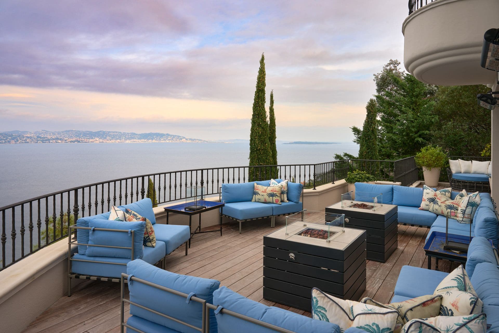 Blue outdoor sofas around a fire pit on a terrace overlooking the sea
