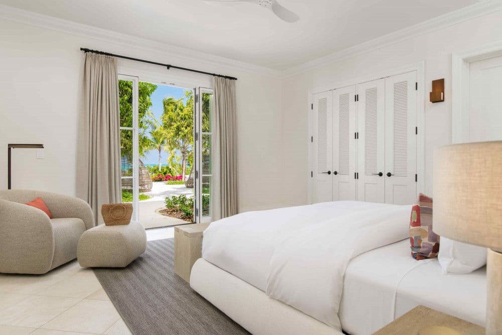 Guest bedroom opening through French doors to a garden path toward the beach at Sea Breeze Estate