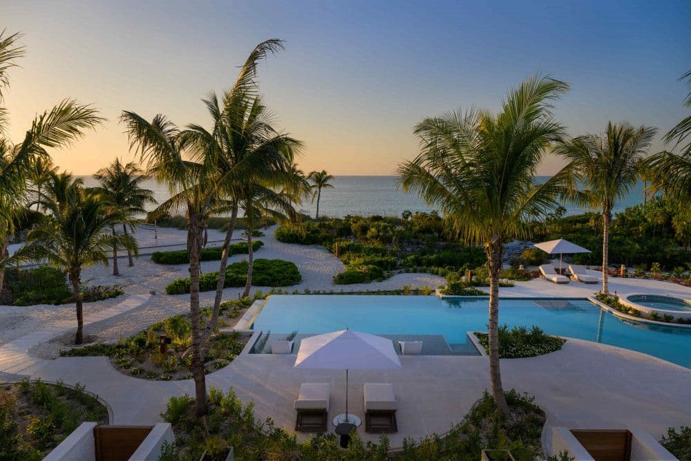 Infinity pool framed by palms with the beach and sunset beyond at Sea Breeze Estate