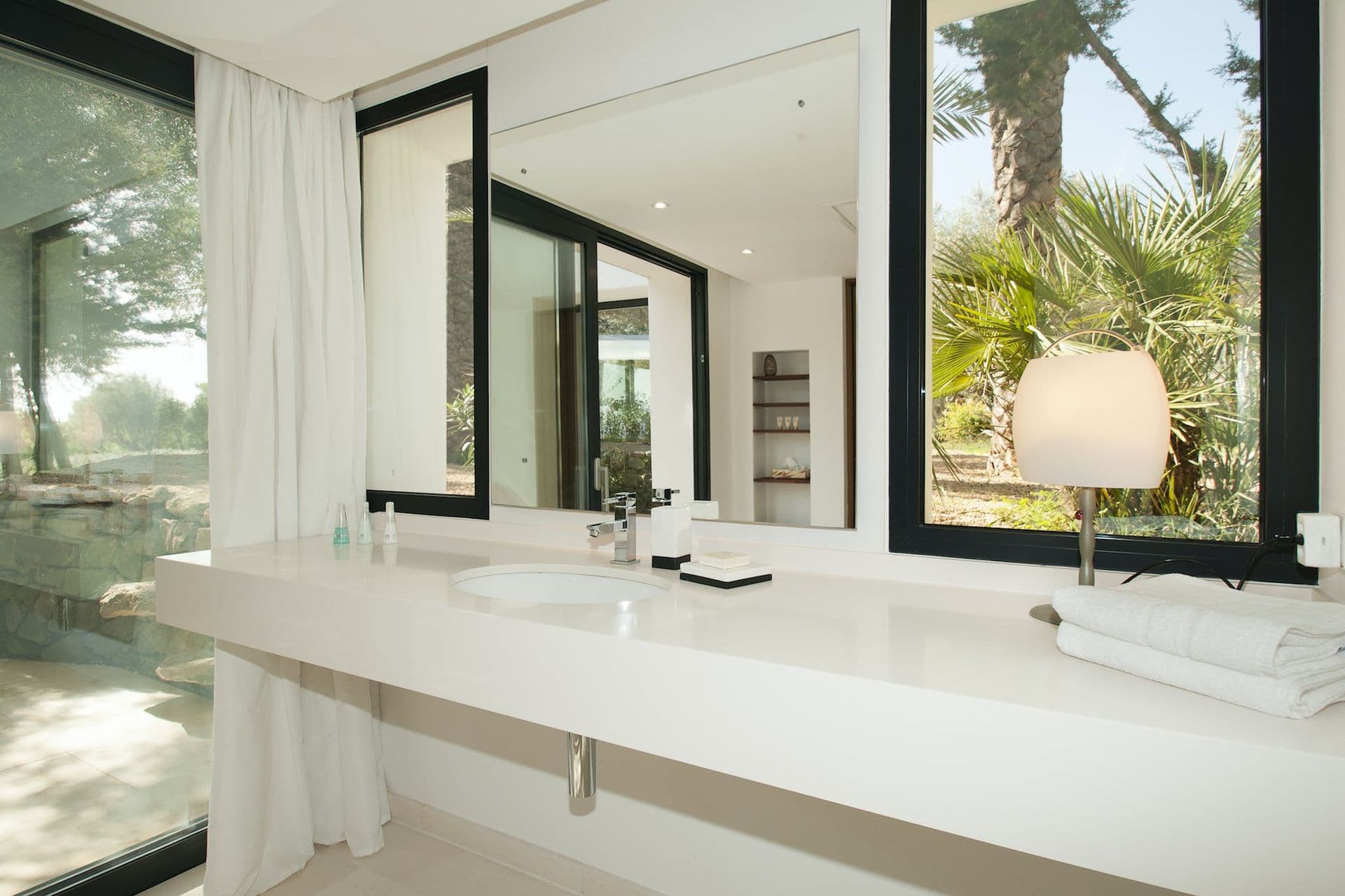 Bathroom with white stone double vanity and mirrored wall reflecting the garden