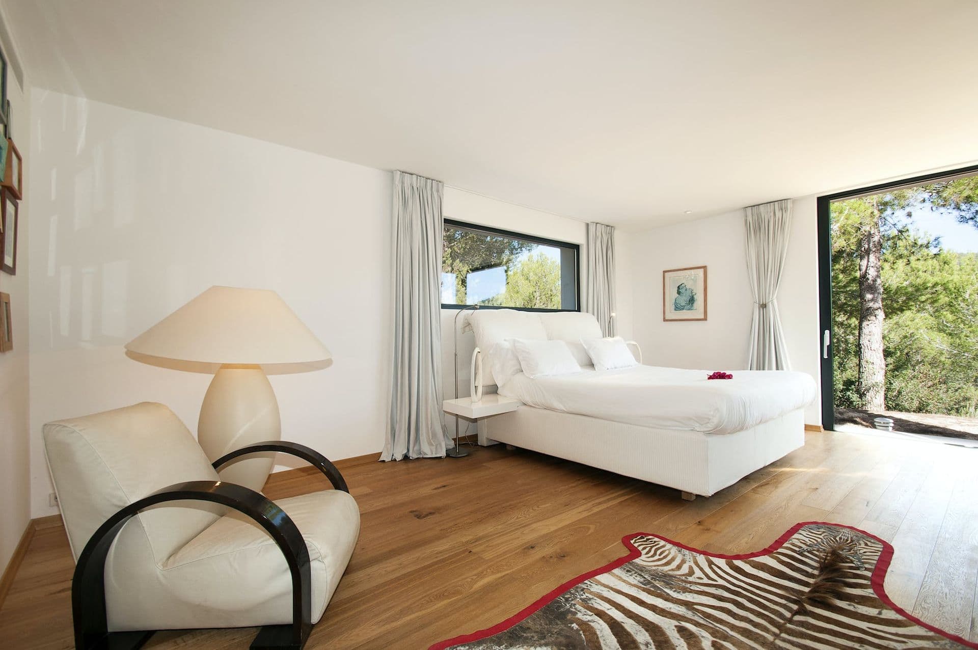 Bright bedroom with white linen bed and wide picture window over the grounds