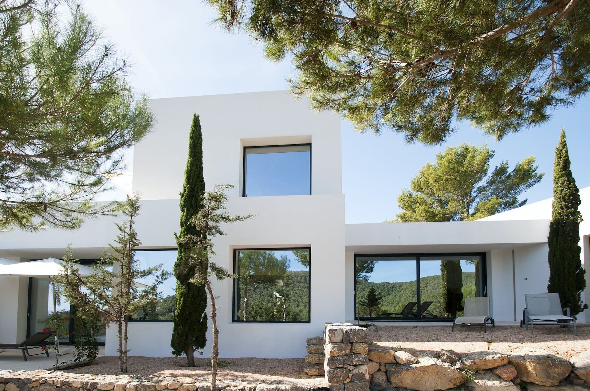 White cubist villa facade at Pure Oasis surrounded by pine and cypress trees