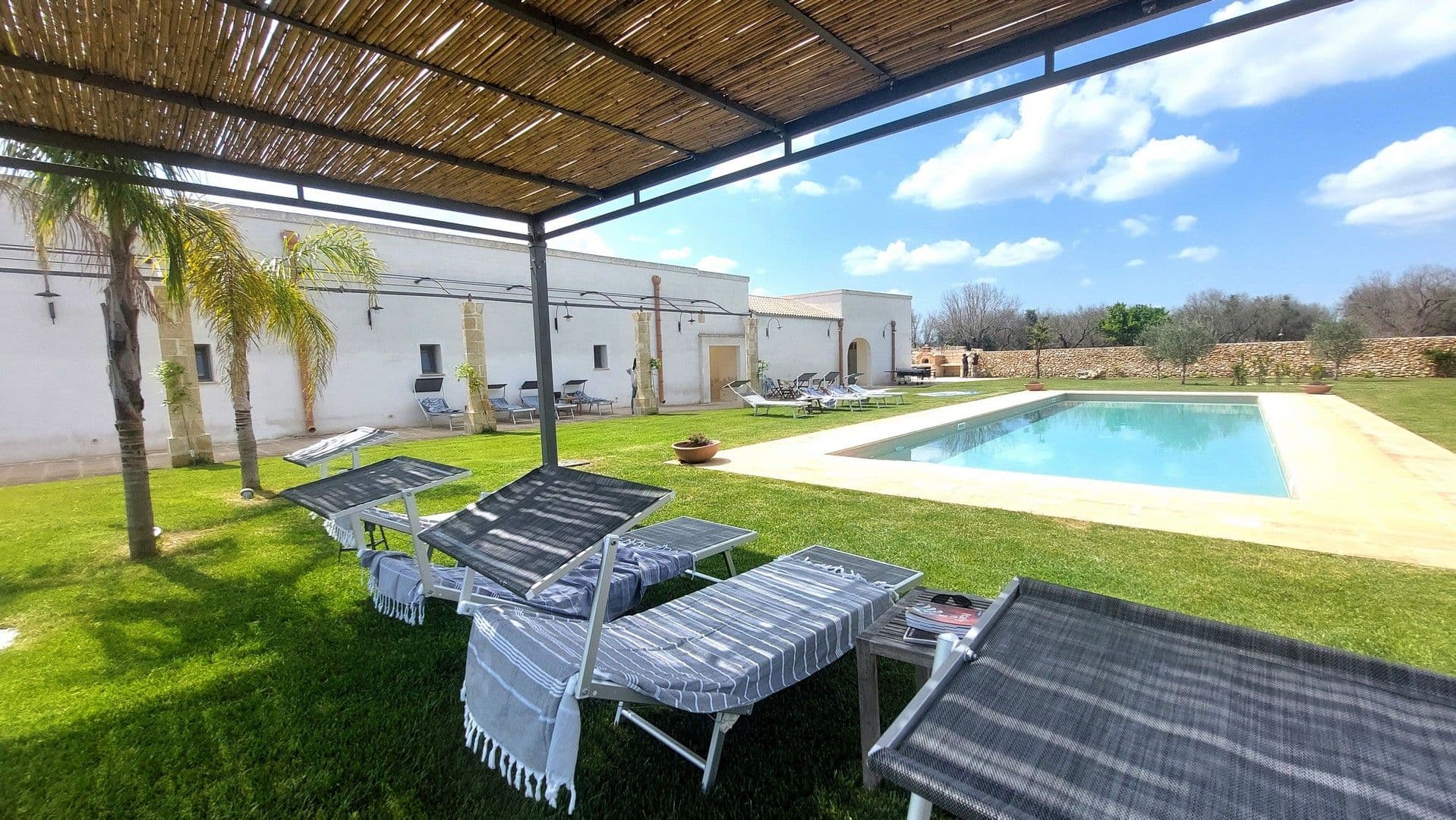 Pool loungers shaded by palm trees at Puglian Farmhouse