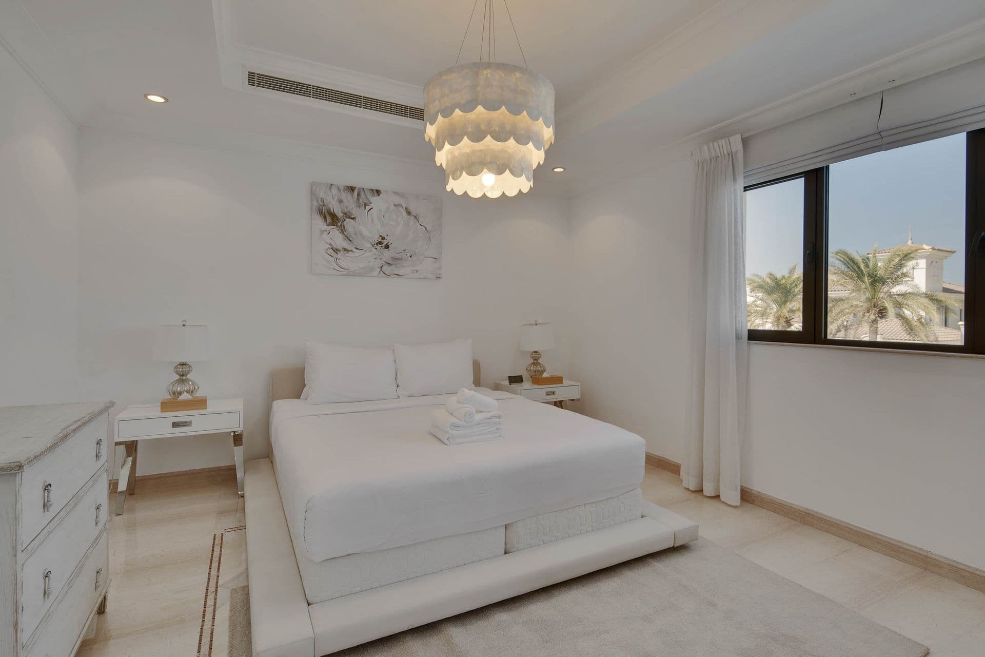 Guest bedroom with a beaded chandelier and warm drapery.