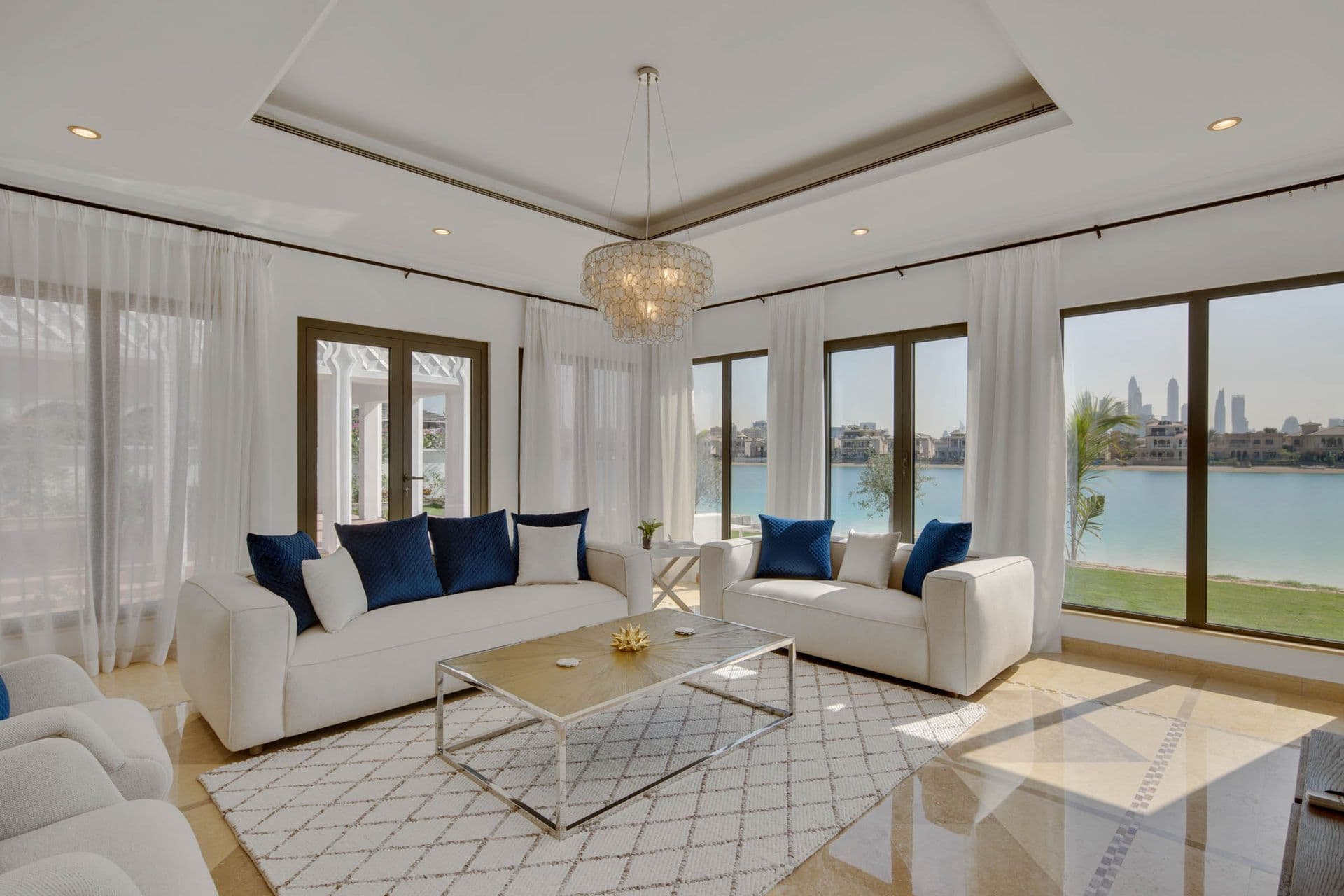 Second living area with white upholstered sofas and floor-to-ceiling windows overlooking the water.