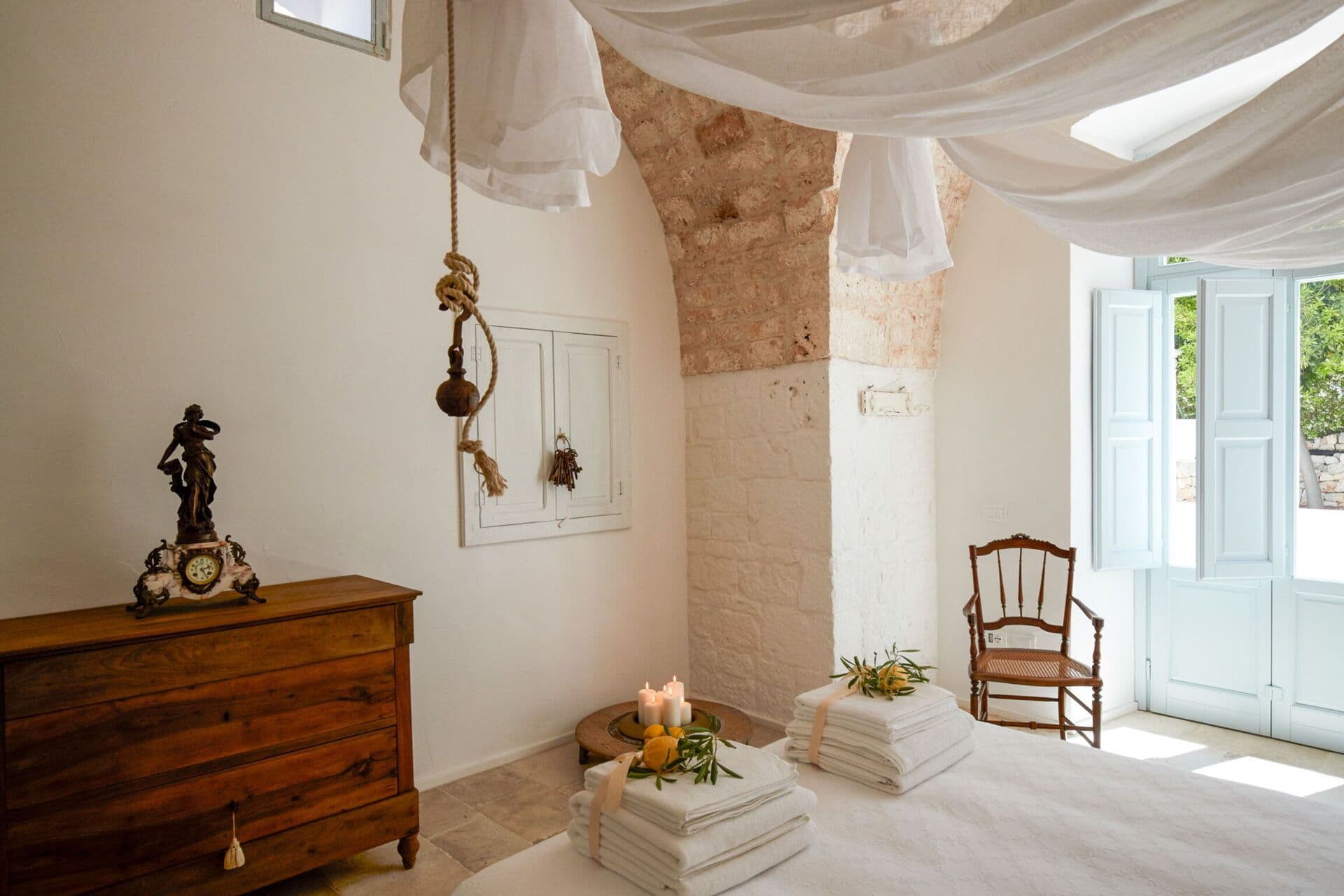 Antique wooden dresser and oval mirror beside a stone niche filled with fresh flowers at Mediterranean Sunhouse