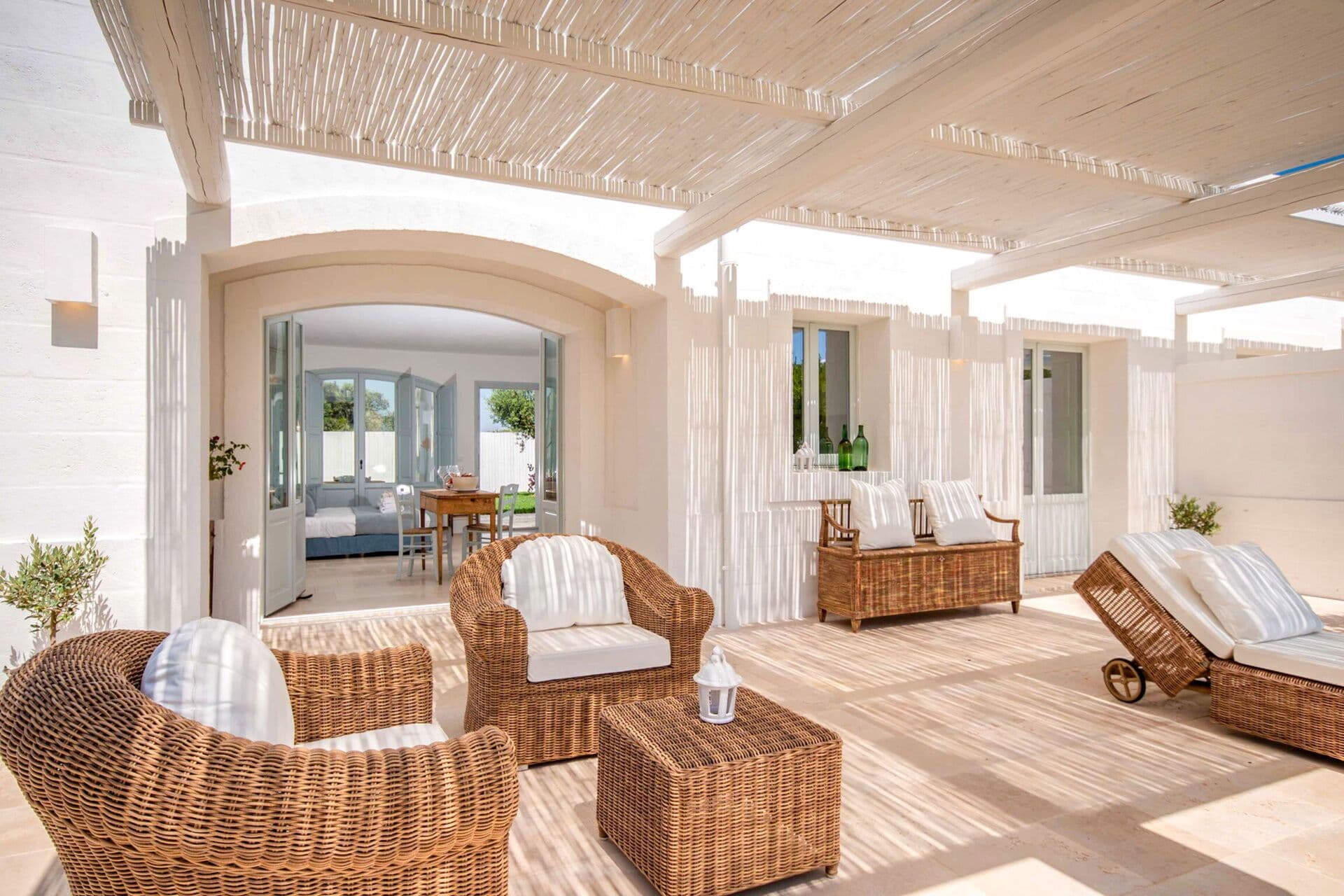 Shaded stone loggia with woven wicker armchairs and a day bed overlooking the garden at Mediterranean Sunhouse