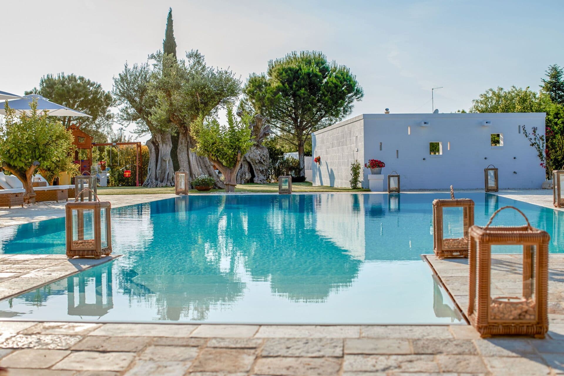 Stone edged swimming pool reflecting olive trees and blue sky in the grounds of Mediterranean Sunhouse