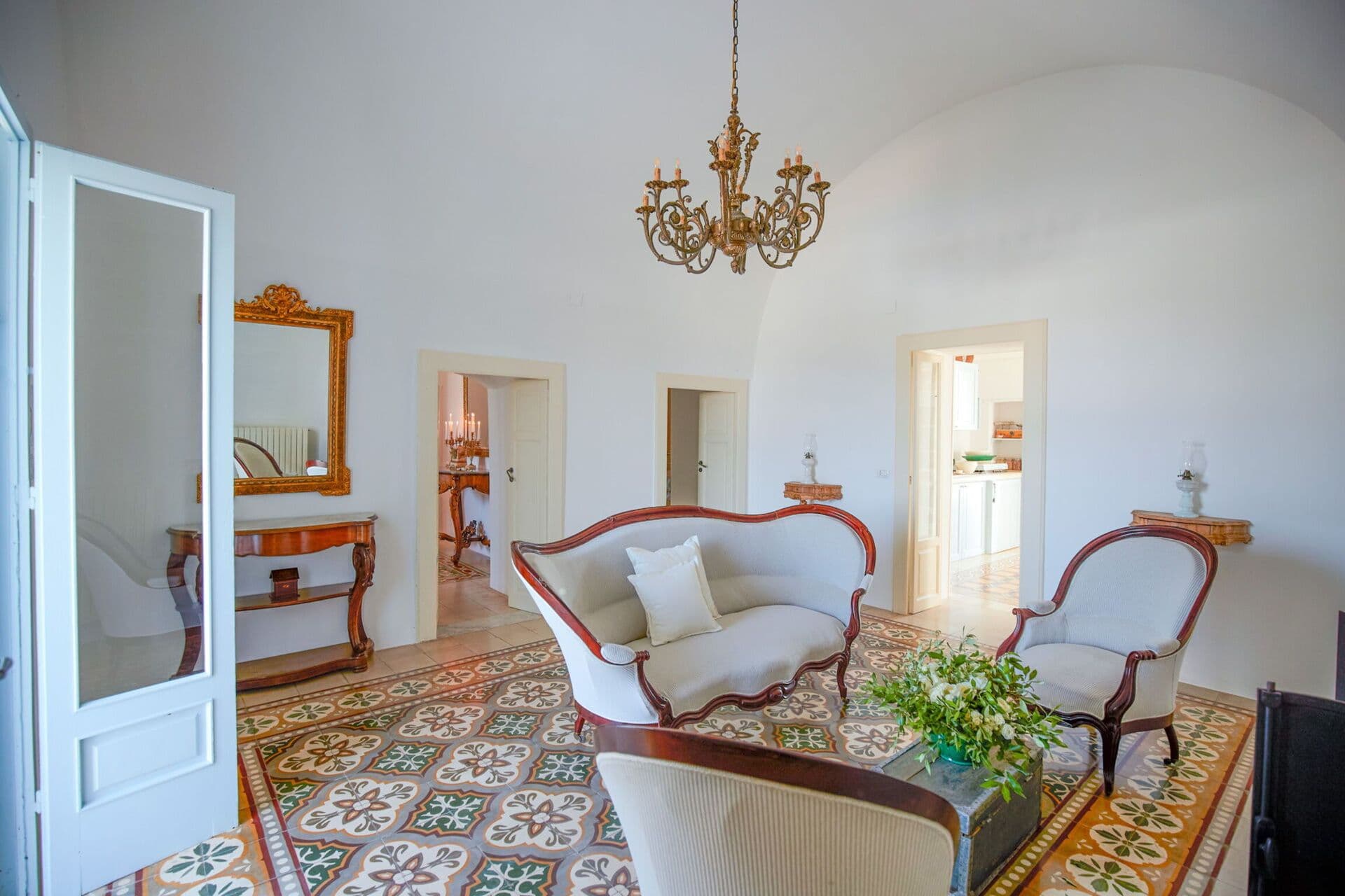 Antique sofa and gilt mirror in a bright reception room with patterned tiled floor at Mediterranean Sunhouse