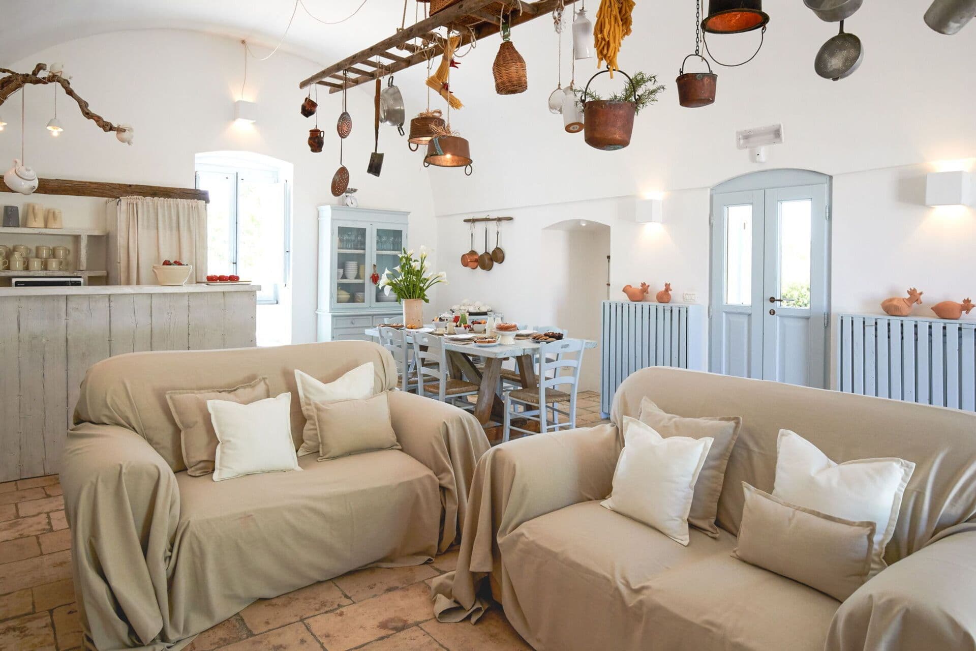 Two linen upholstered sofas beneath a rustic beamed ceiling hung with copper pots at Mediterranean Sunhouse