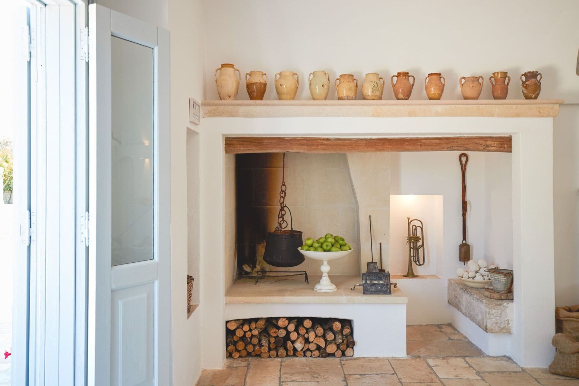 Traditional whitewashed stone fireplace nook lined with terracotta jugs in the vaulted living space at Mediterranean Sunhouse