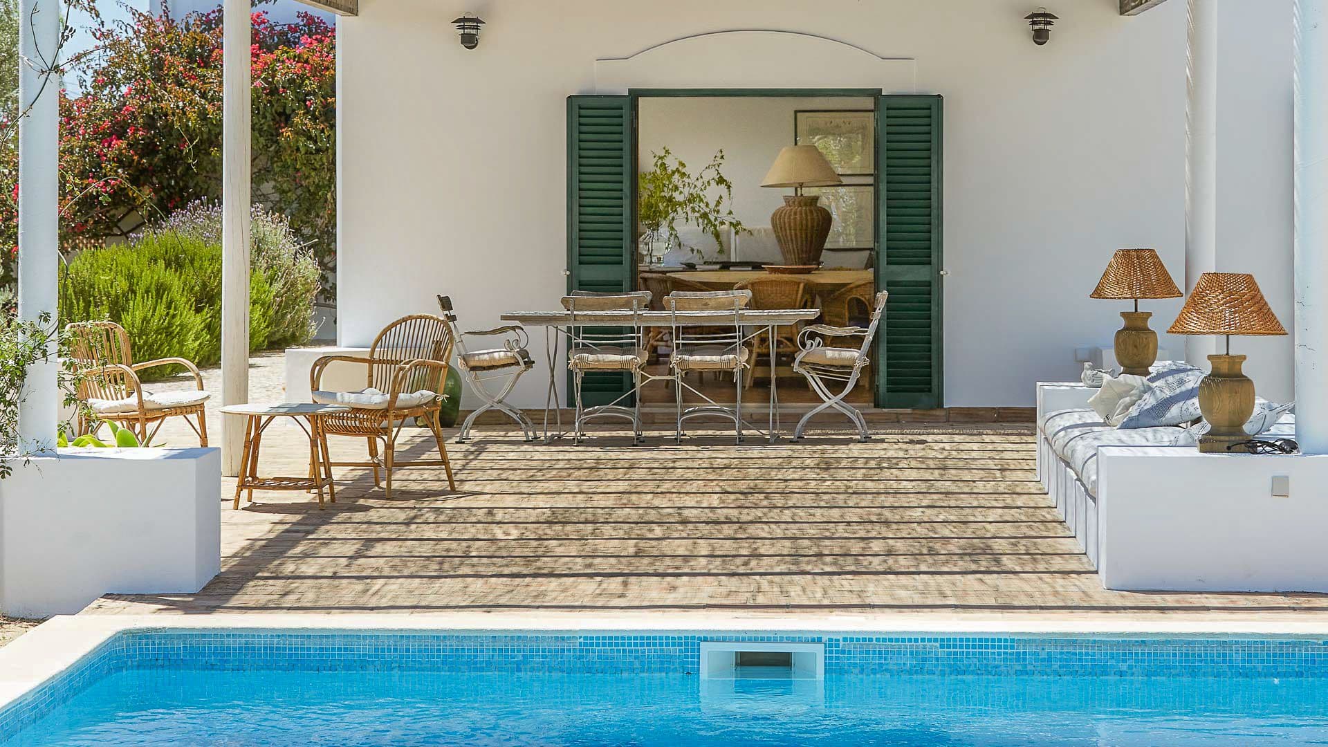 Poolside terrace with a rattan dining set beneath green-shuttered windows
