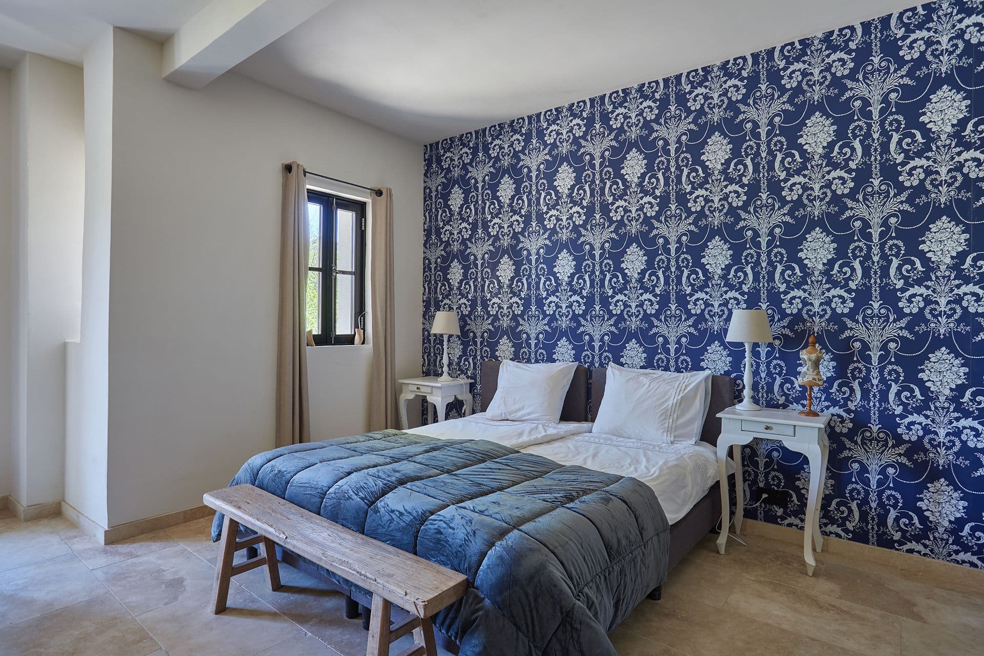 Bedside view of the damask-walled double bedroom with matching lamps and a rustic bench at A Glass of Champagne, Provence