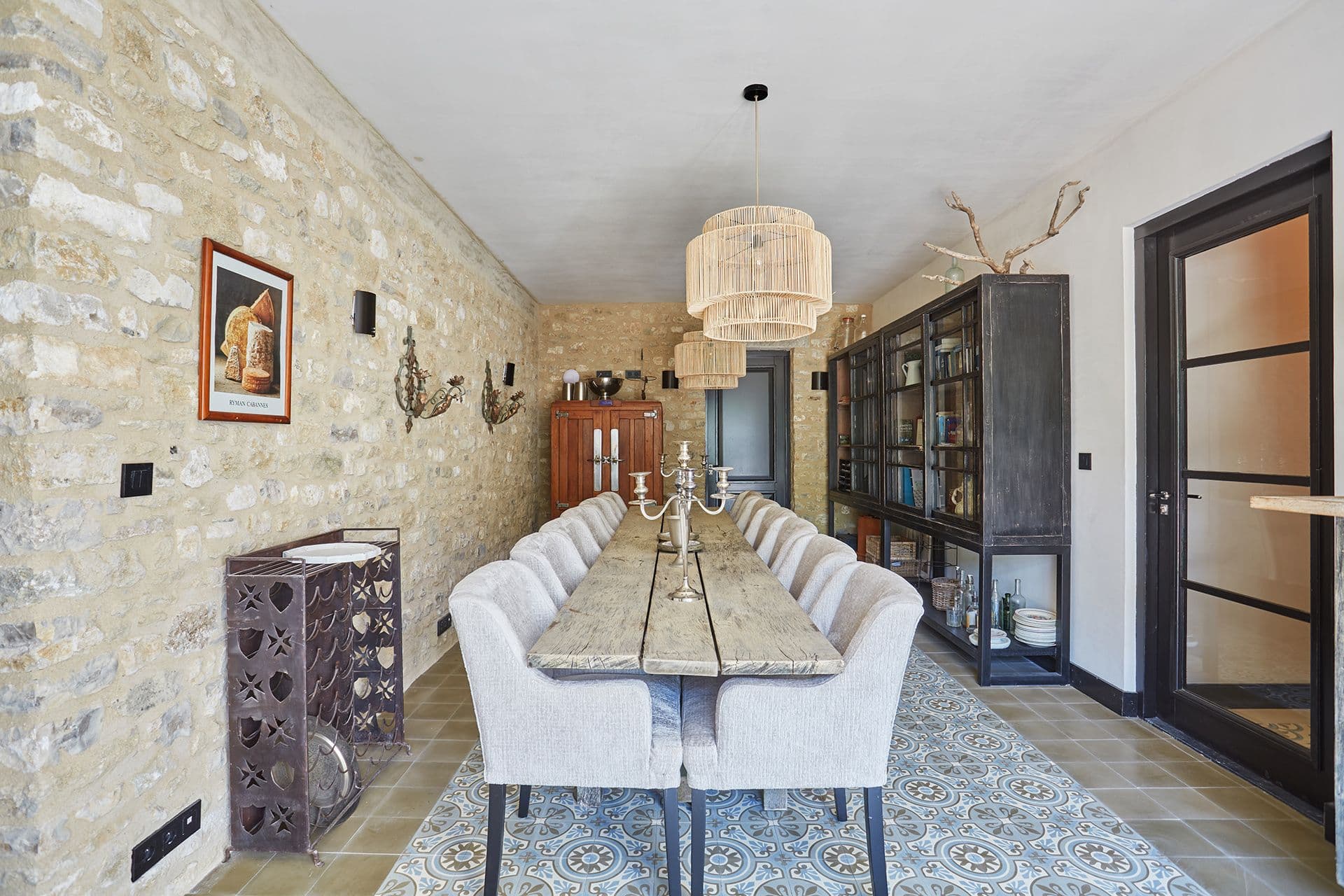 Formal dining room with patterned encaustic-tile floor and a glazed cabinet against exposed stone at A Glass of Champagne, Provence