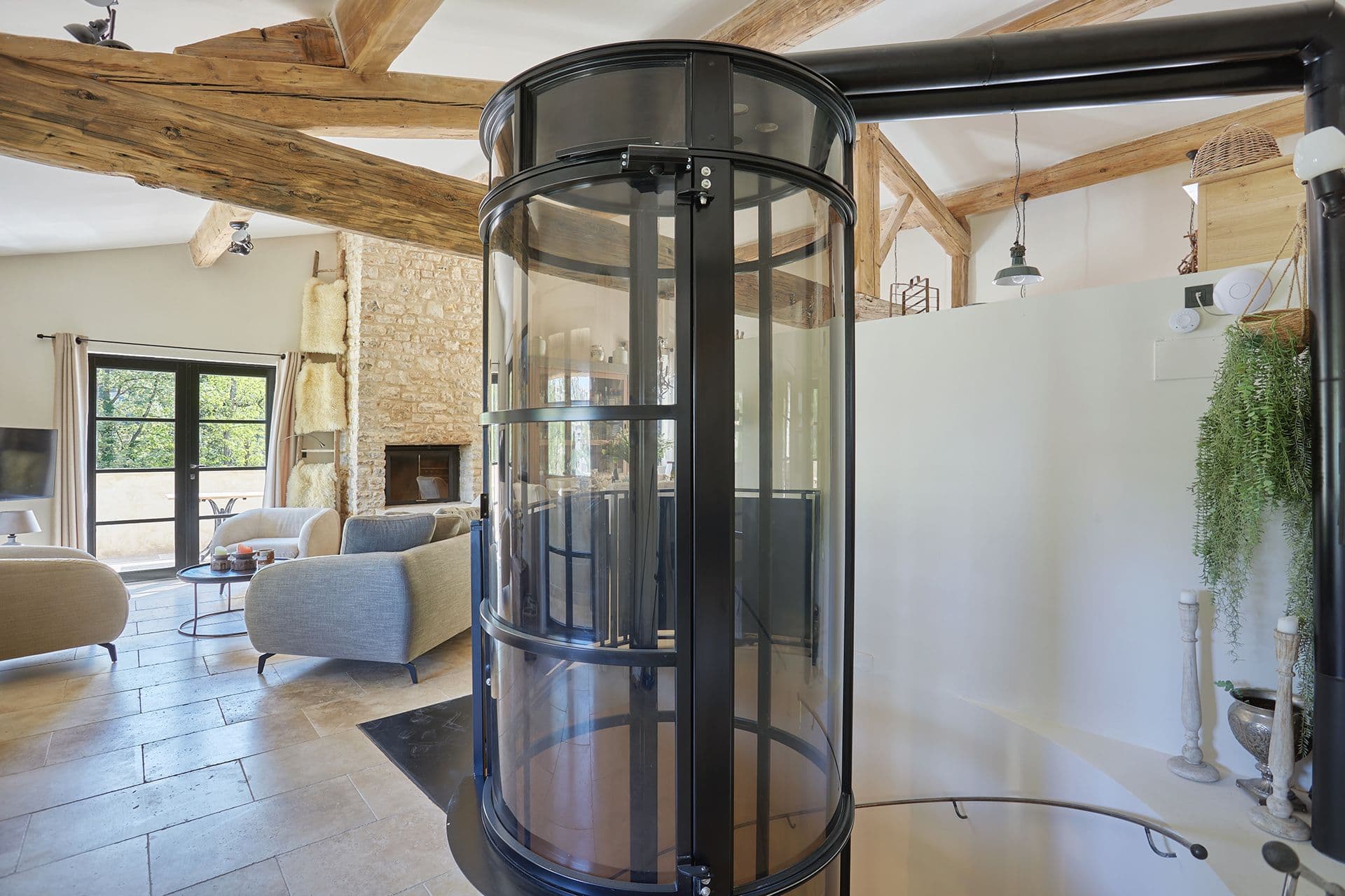 Circular glass passenger lift set within the beamed open-plan living space at A Glass of Champagne, Provence
