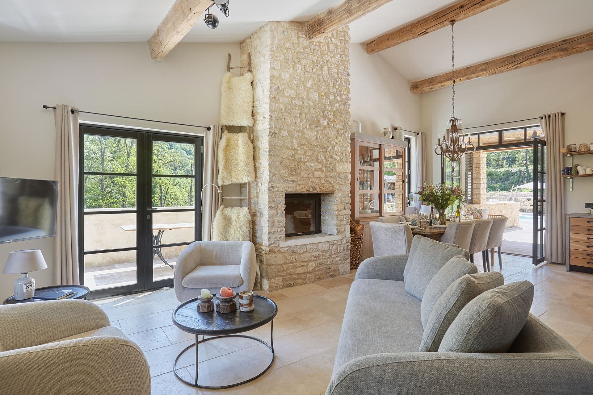Beamed living room with a dressed-stone fireplace, linen sofas and a chandelier at A Glass of Champagne, Provence