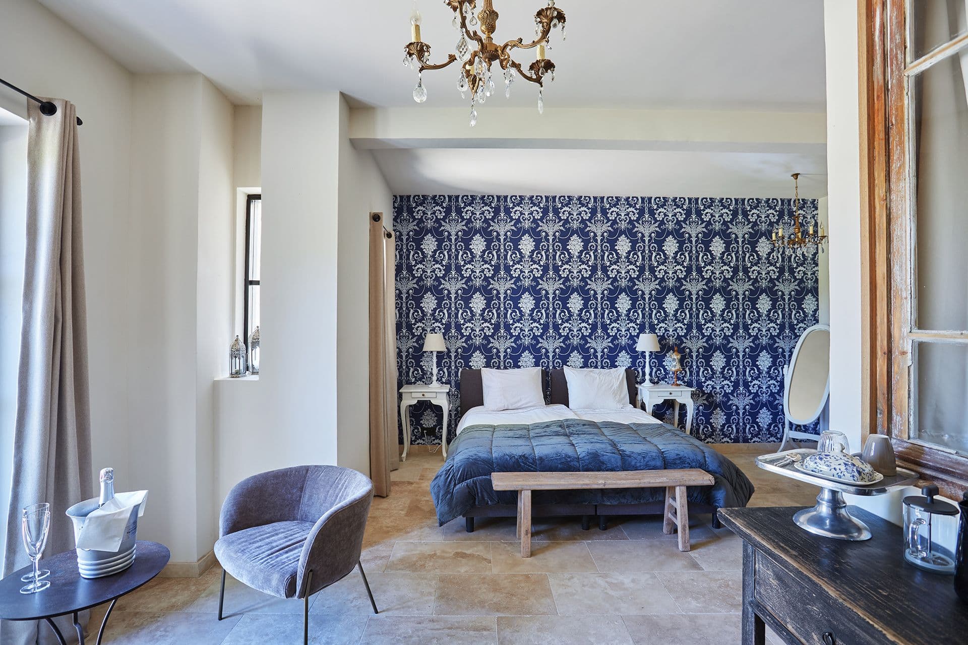 Double bedroom with a blue-and-white damask feature wall, chandelier and travertine floor at A Glass of Champagne, Provence