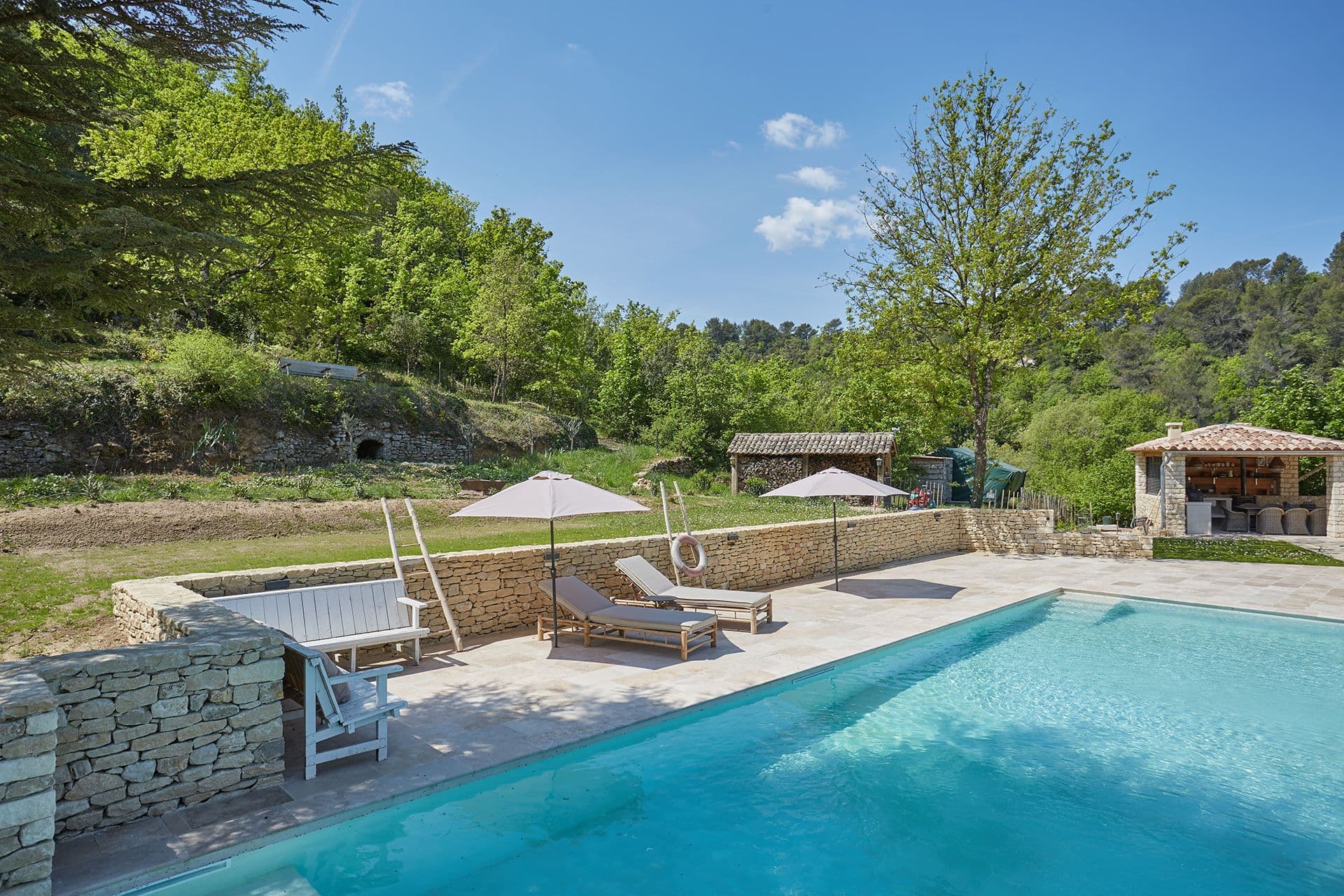 Poolside loungers, dry-stone walls and a stone summer-kitchen pavilion in the garden at A Glass of Champagne, Provence