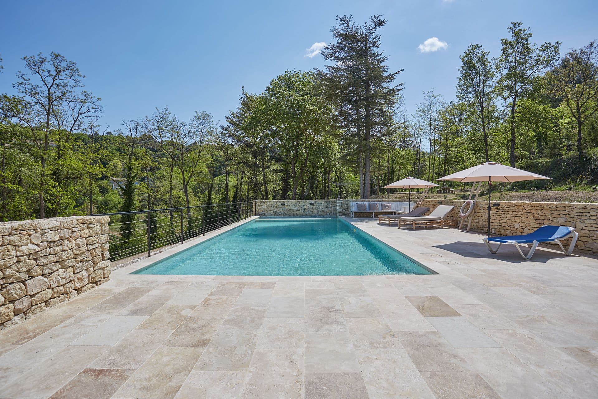Infinity-edge swimming pool and travertine sun terrace at A Glass of Champagne, framed by Luberon woodland in Provence