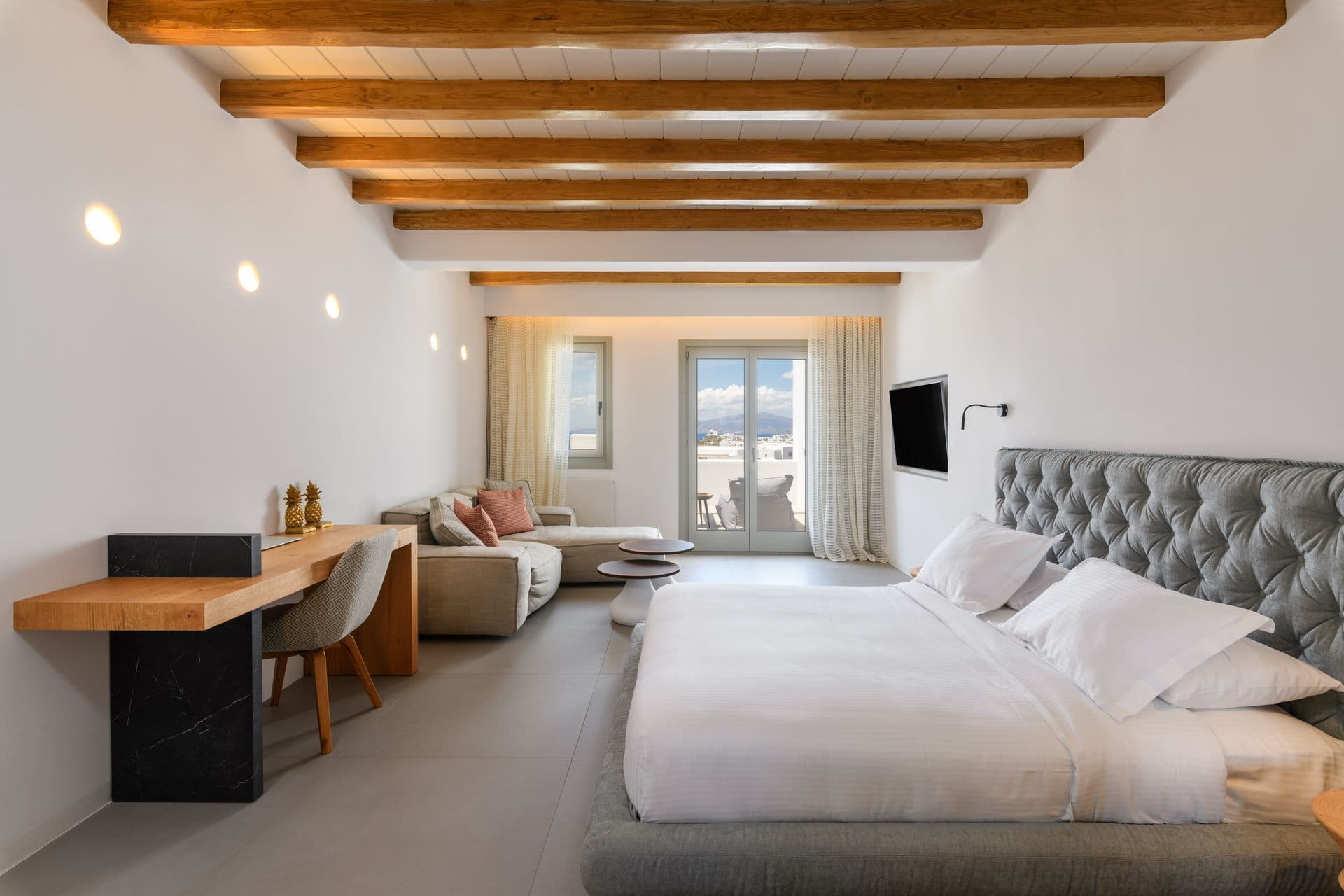 Double bedroom with a grey tufted headboard and a desk by the window at Cycladic Sunset Stay, Mykonos