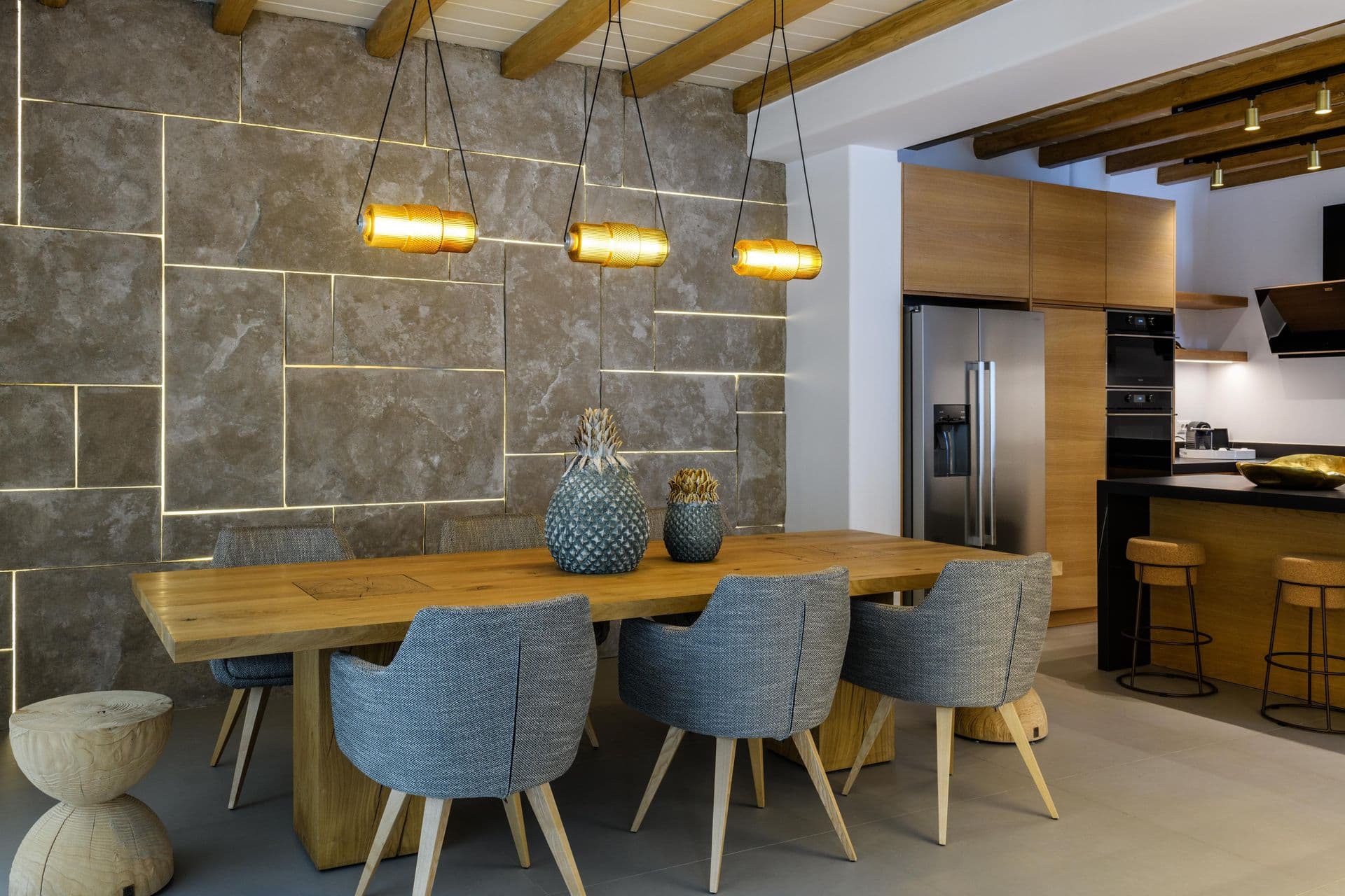 Dining table with blue chairs against a stone wall under linear pendants at Cycladic Sunset Stay, Mykonos