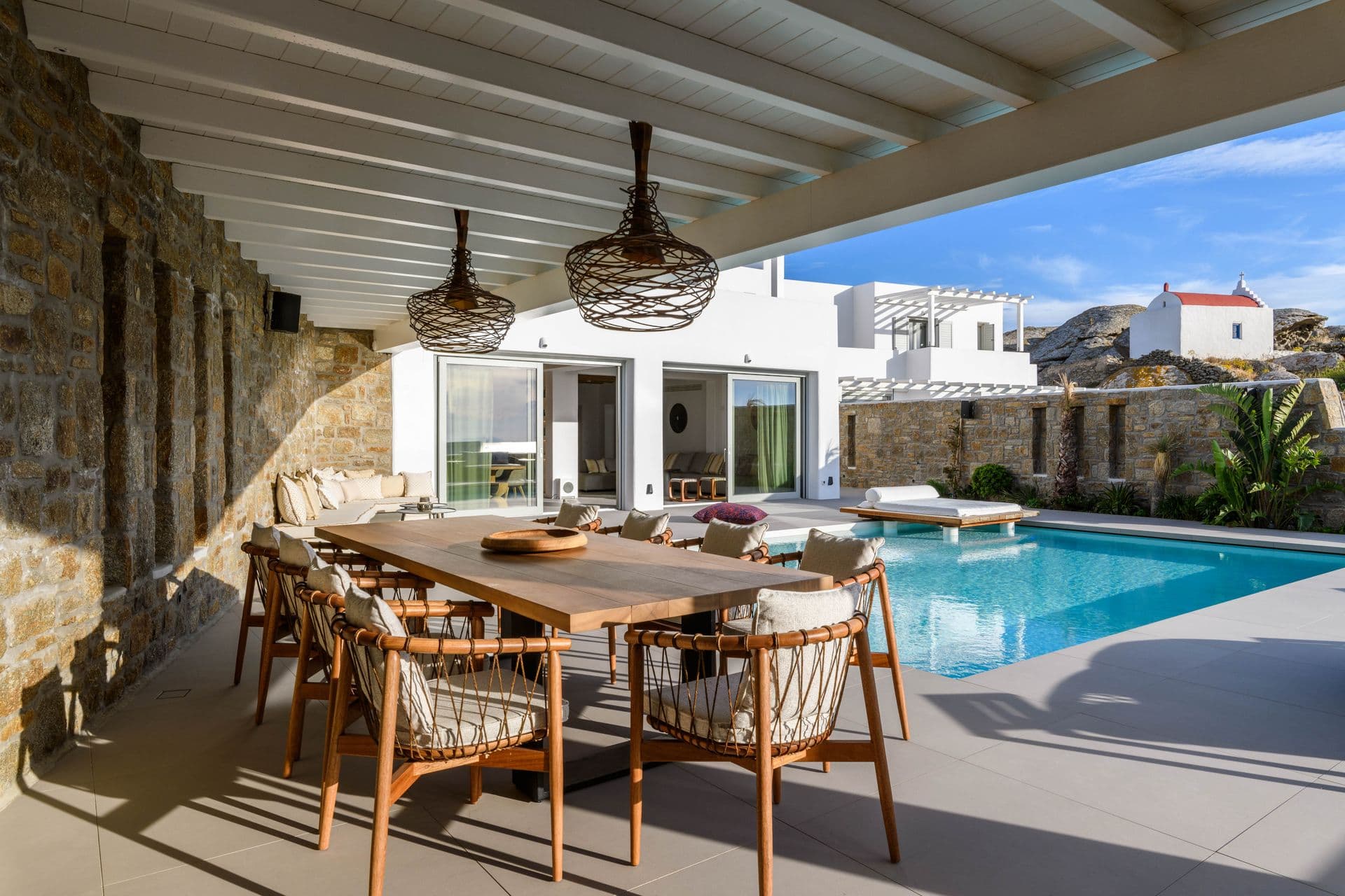 Outdoor dining table beneath a timber pergola beside the pool and sea at Cycladic Sunset Stay, Mykonos