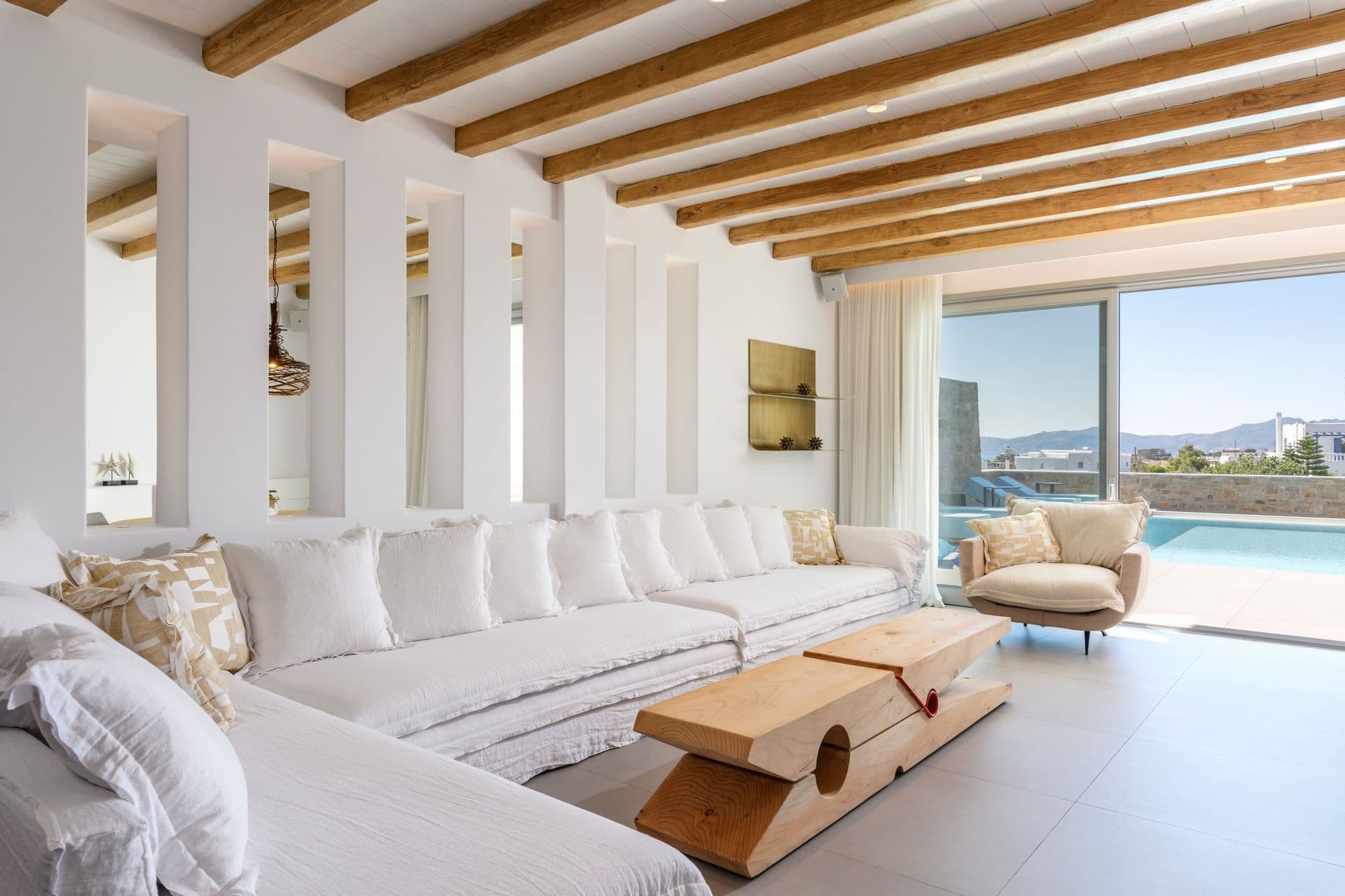 Living room with white sofas under timber beams opening to the pool at Cycladic Sunset Stay, Mykonos